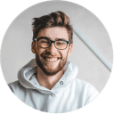 Jeune homme souriant aux lunettes noires, portant un sweat à capuche blanc, symbolisant la collaboration pour la création.