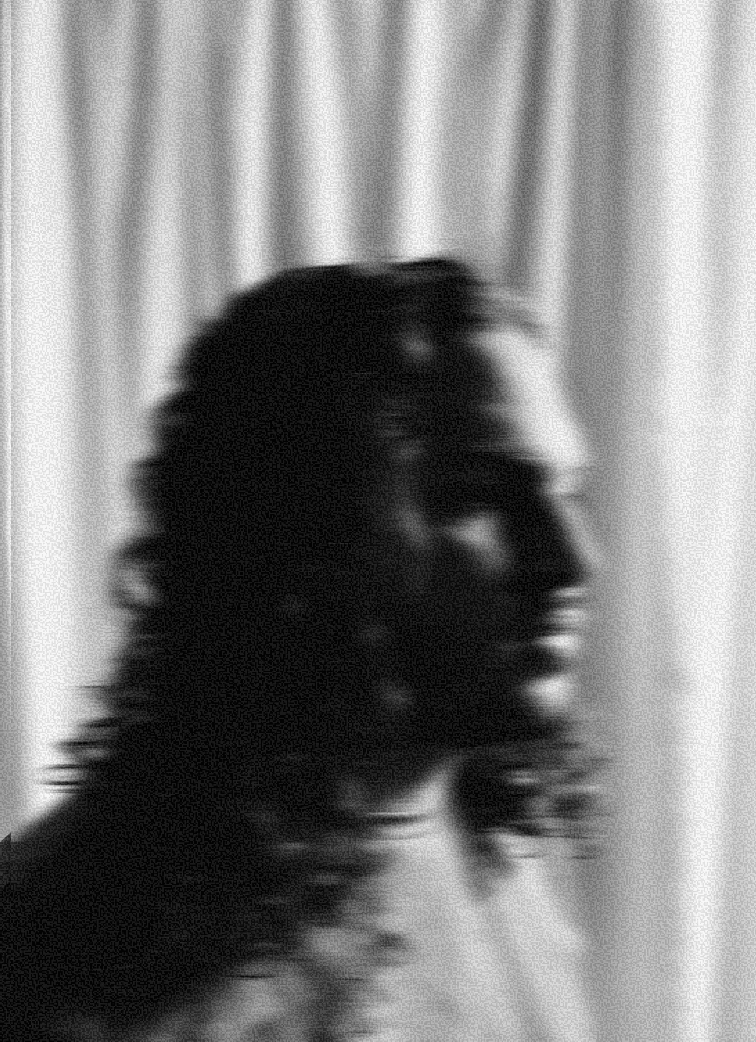 A thoughtful young person with dark hair gazes to the side, captured in soft black and white lighting.