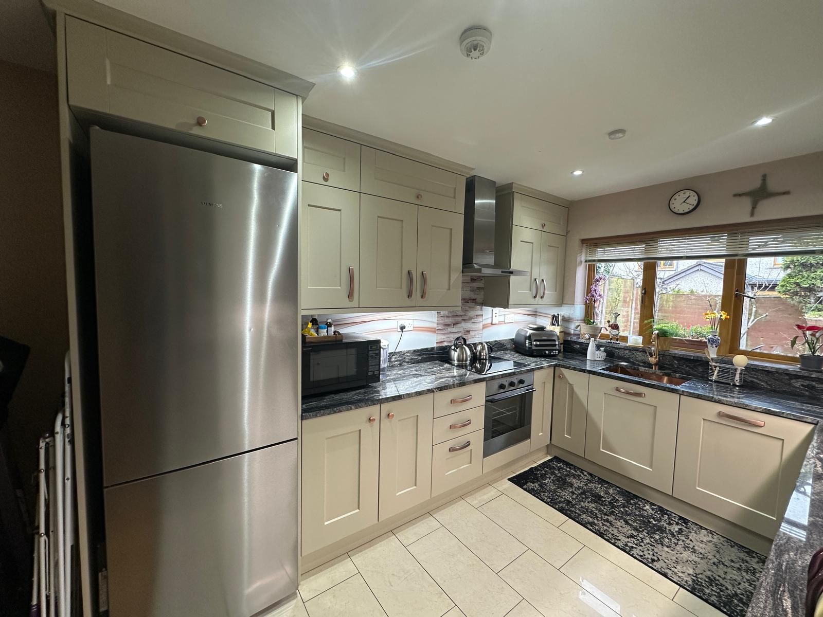 Modern two-story home with large glass windows, warmly lit interiors, and a balcony. Surrounded by trees and a manicured lawn at dusk. Cozy ambiance.