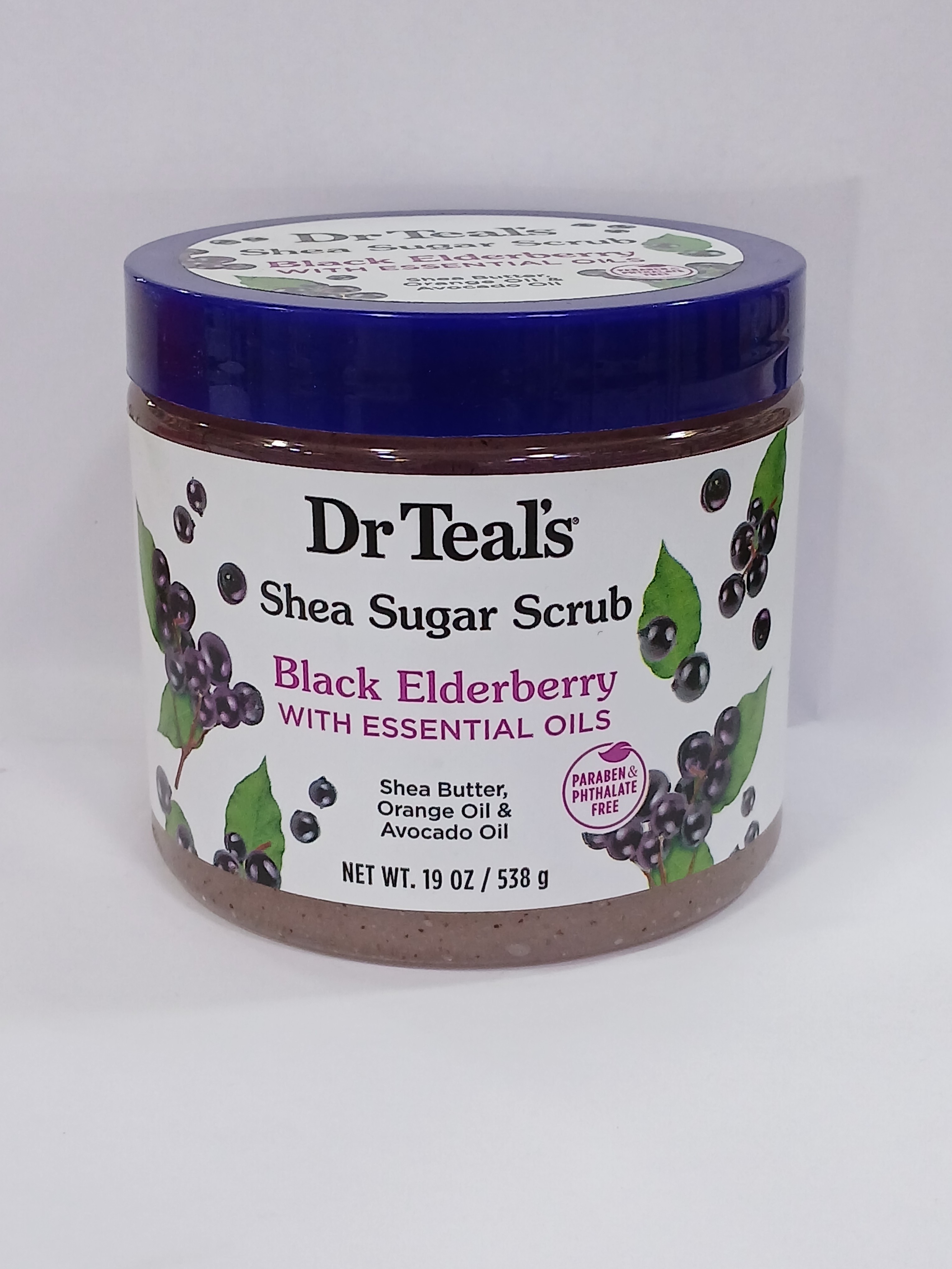 A round jar with a blue lid and white label featuring black elderberry graphics sits against a plain background, containing a coarse brown sugar scrub mixture.