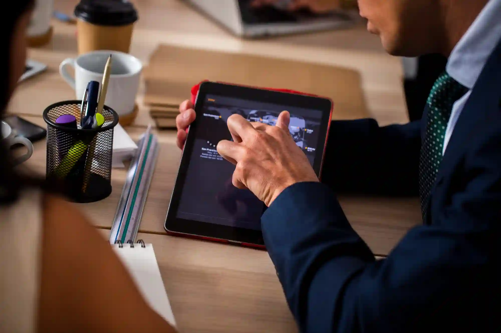 A professional in a suit uses a tablet to present digital content to a colleague during a business meeting.