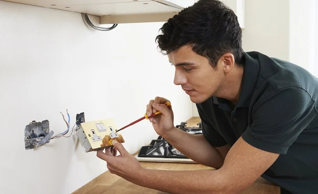 Electrician repairing wall electrical outlet and connecting wiring with screwdriver