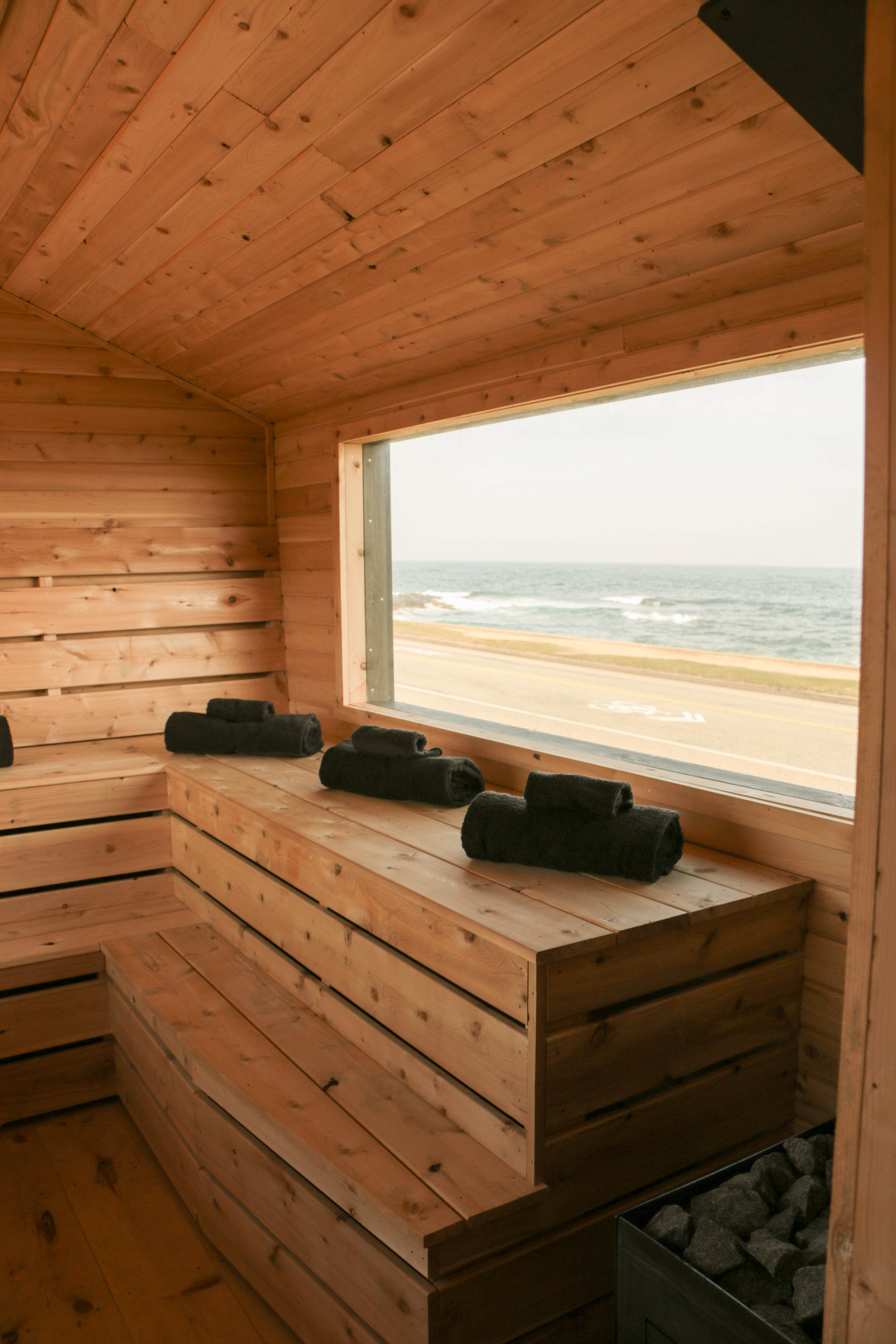Interior of a cedar wood-fired mobile sauna with tiered benches and panoramic window overlooking a winter landscape.