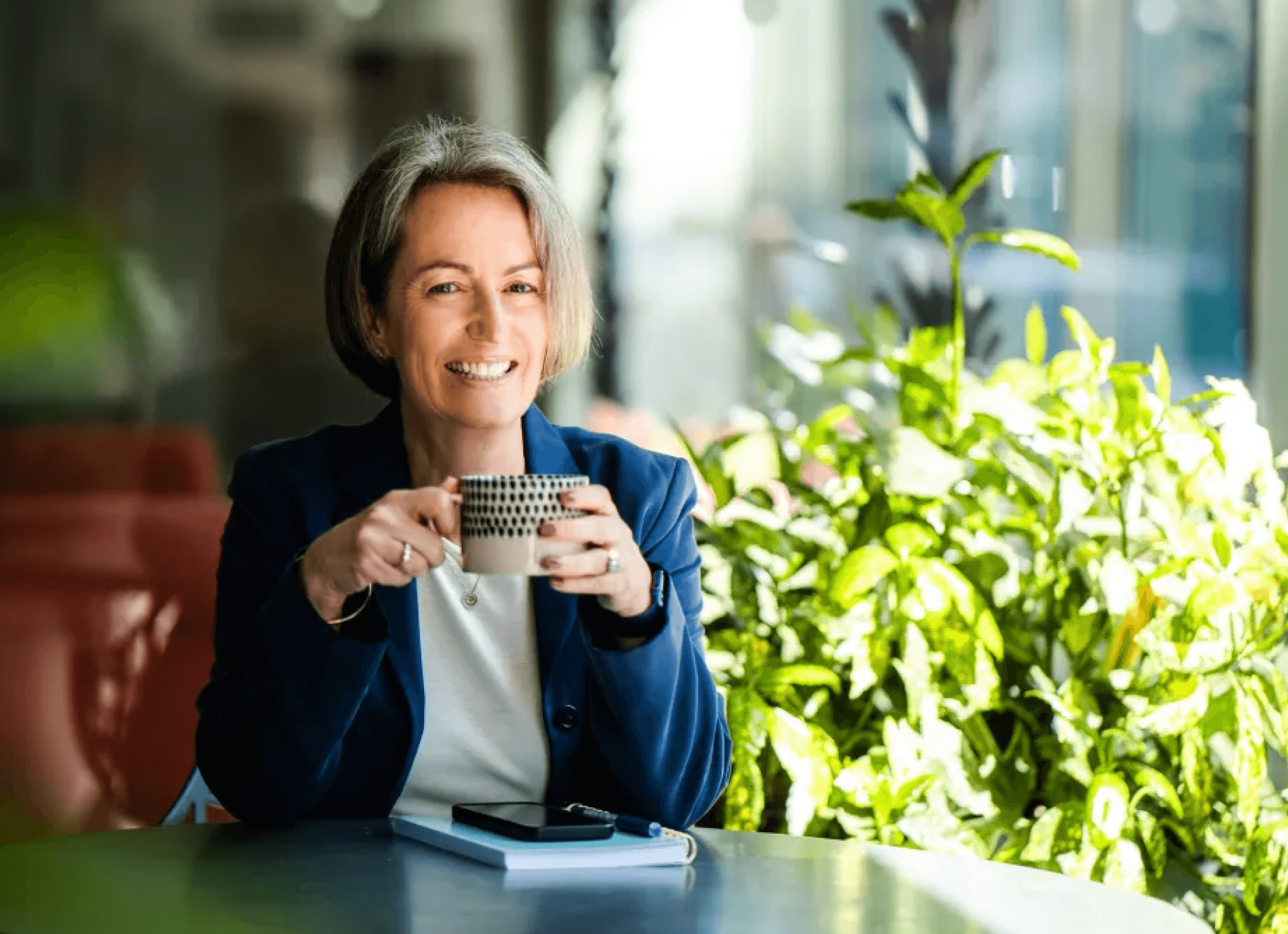 Kate sitting with her tea cup in hand with some greenery in the background