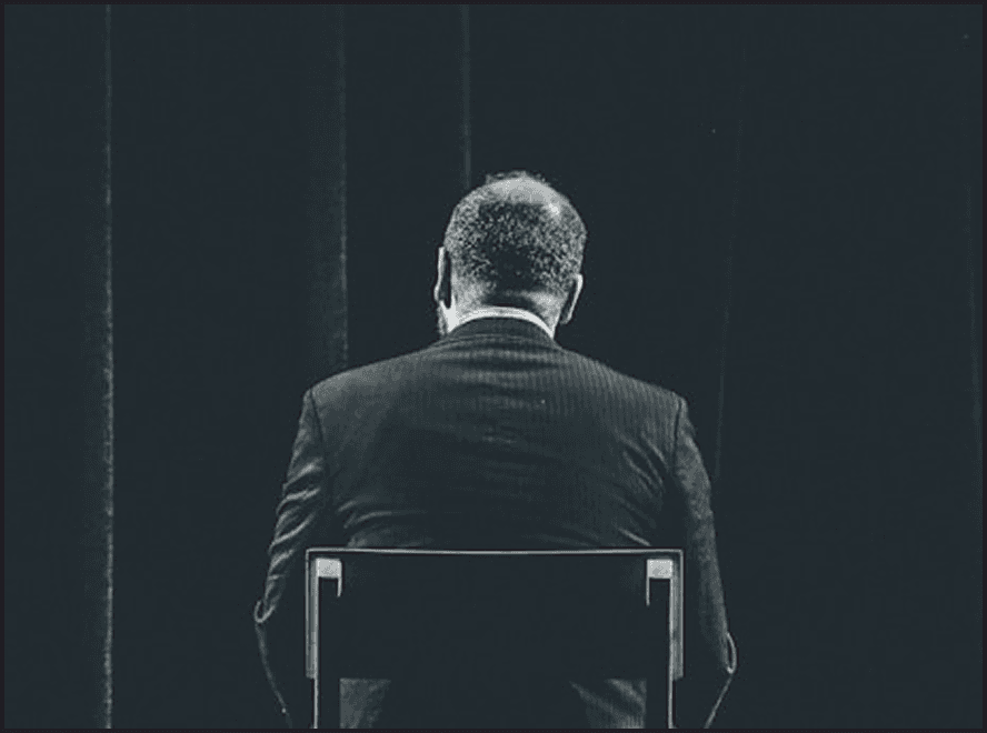 Person in pinstripe suit seated with back to camera