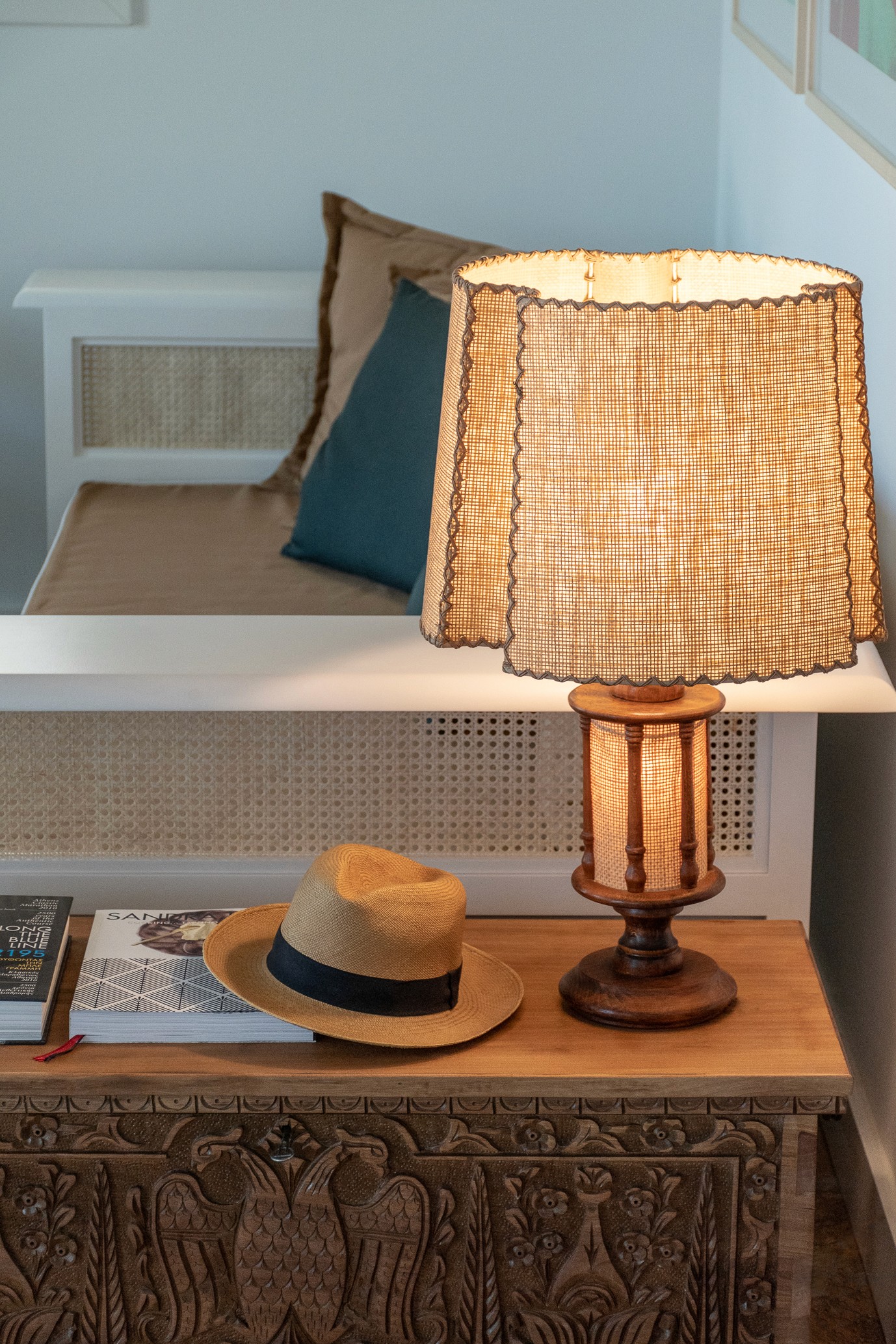 A lamp on a sidetable next to a hat resting on top of a book