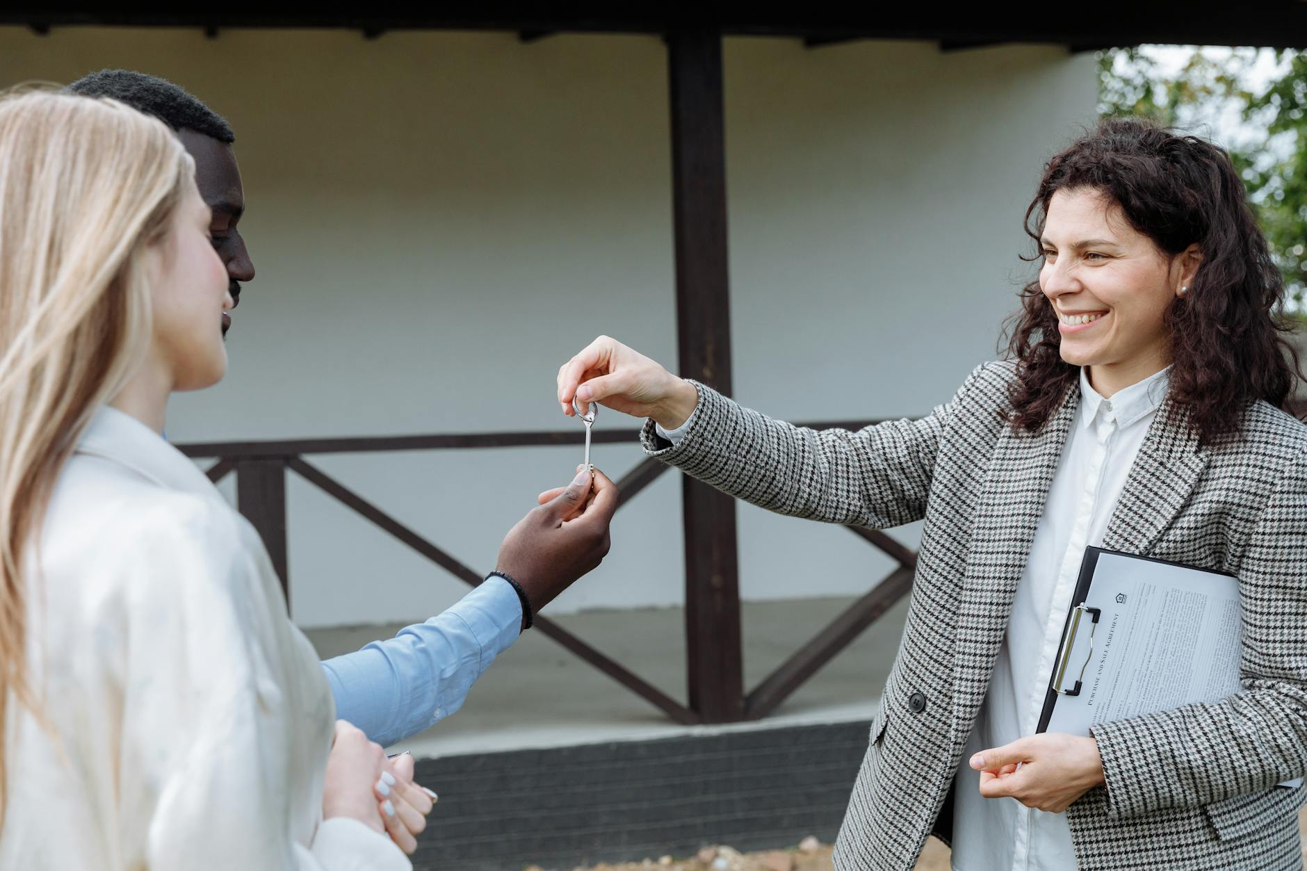 Smiling estate agent in a grey checked blazer handing property keys to a couple standing outside a building
