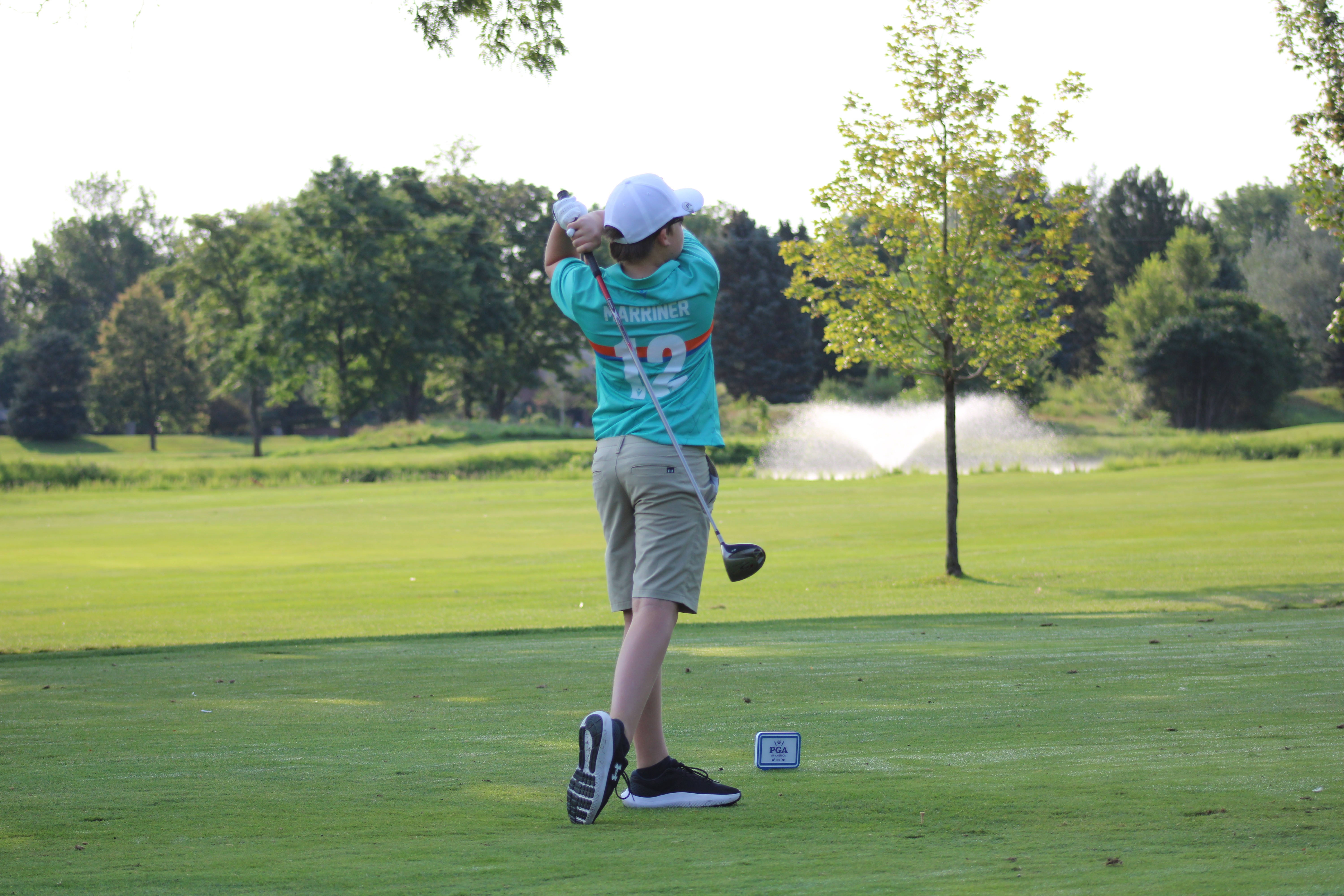 A group of students at the edge of a green, chipping balls towards net targets.