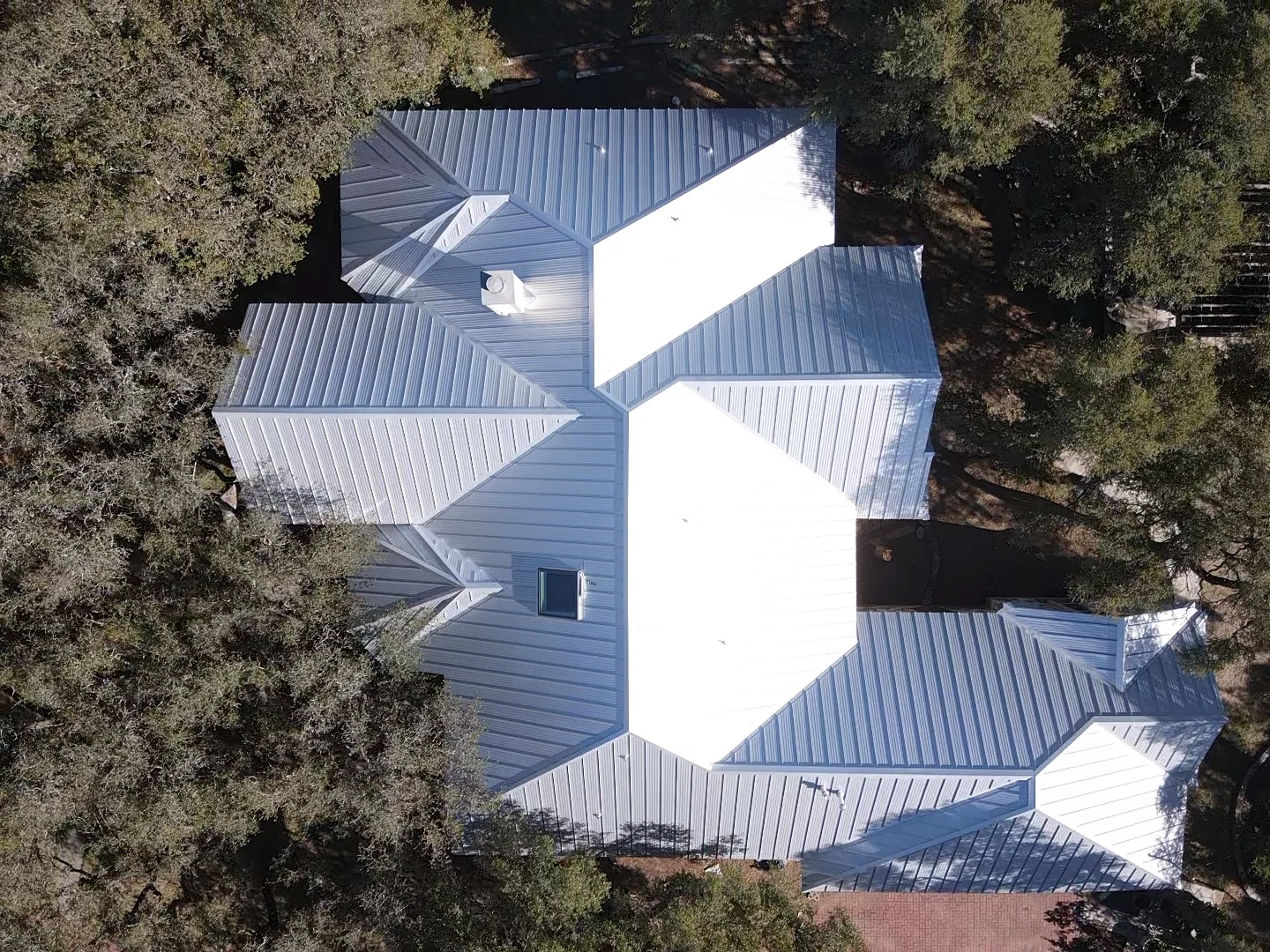Silver-colored standing-seam metal roof with multiple hips and valleys, a chimney and a rectangular skylight.