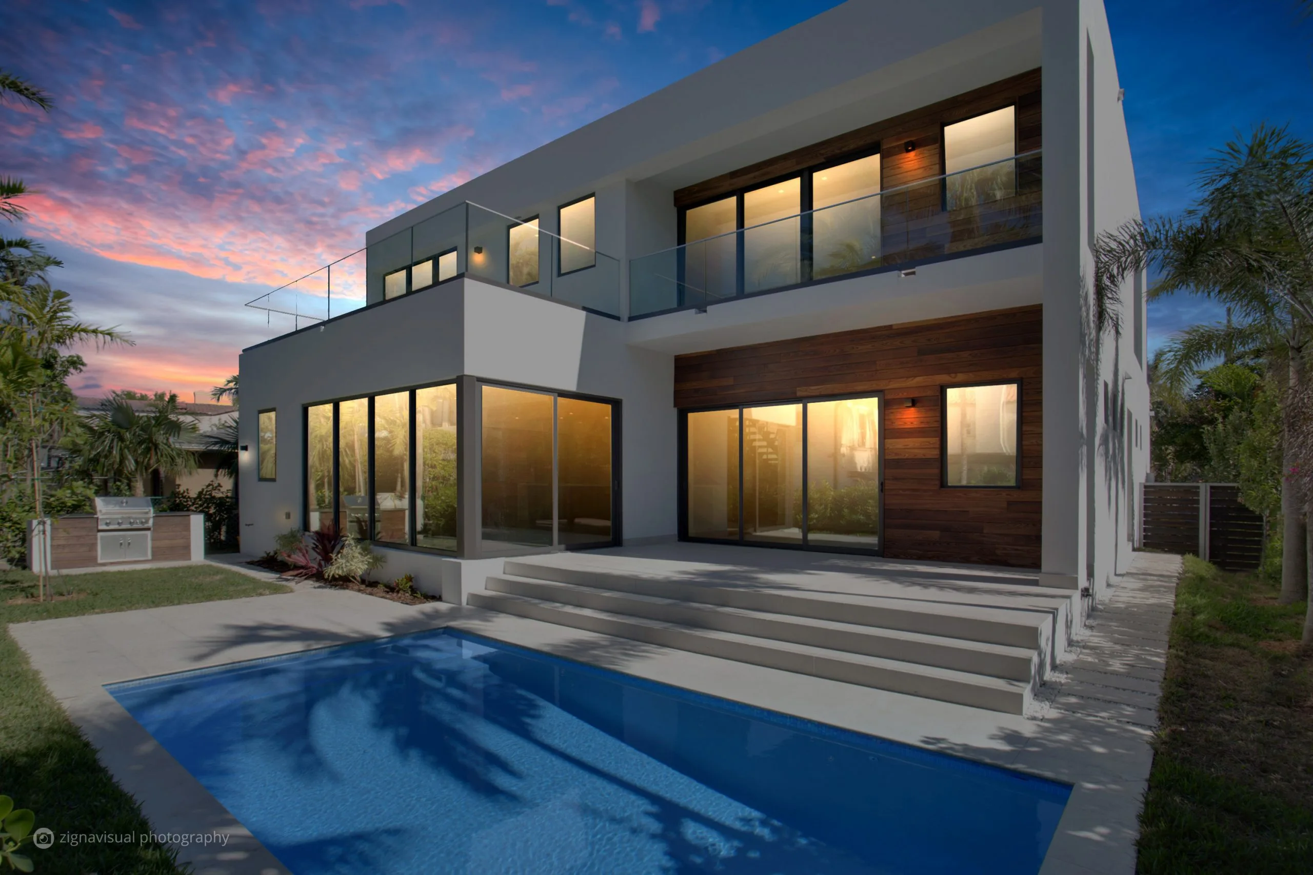 Rear view of modern two-story Miami Beach home with pool and wood cladding at sunset