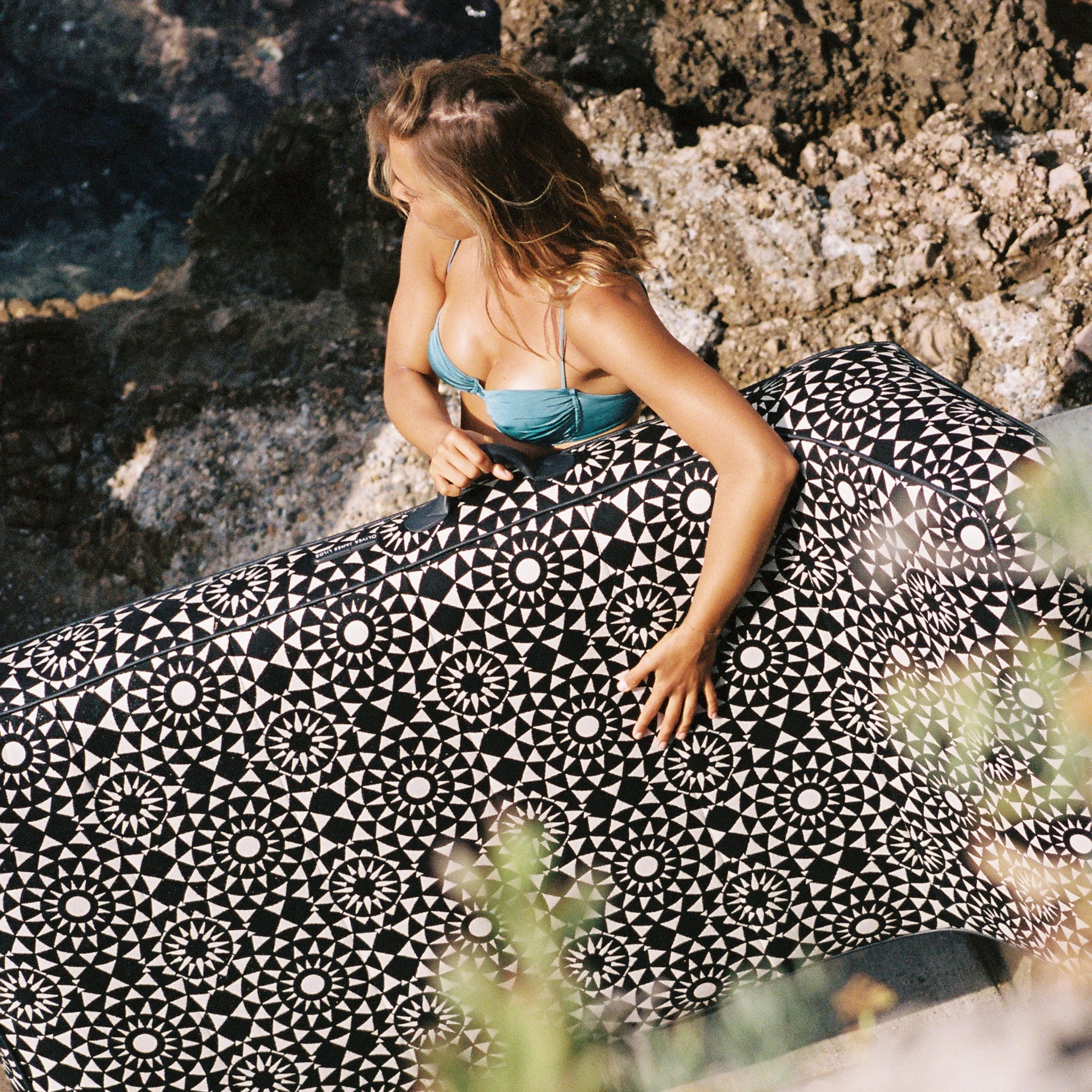 Woman carrying a luxury black-and-white geometric pool float on a rocky coastline
