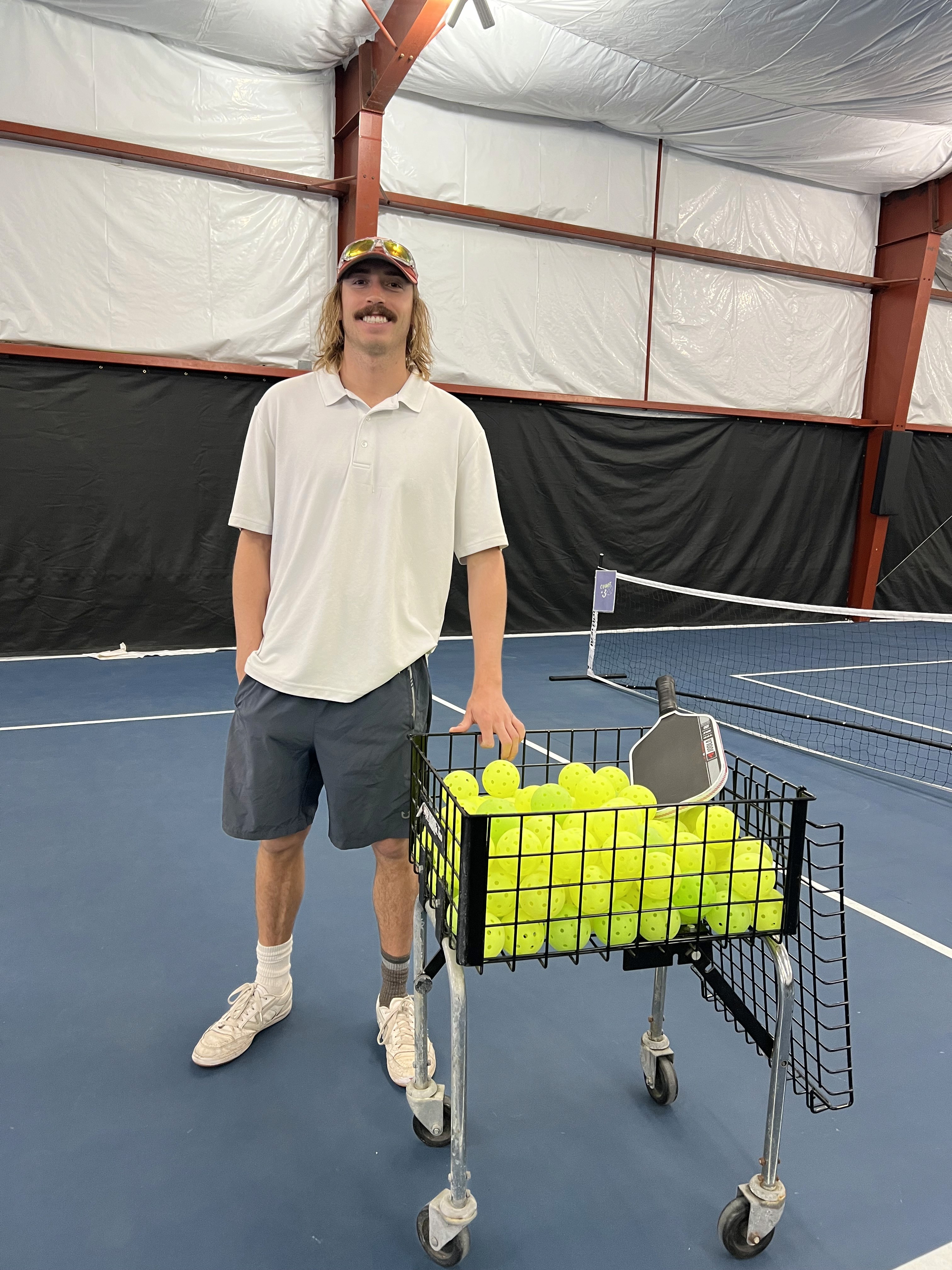 Instructor Devin McCausland beside a basket of pickleballs