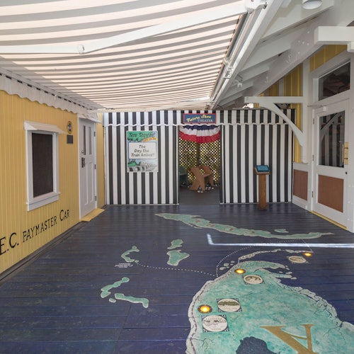 An indoor area with yellow and white striped walls, a map of the Bahamas on the floor, and a sign reading "Bahamian Welcome Center."