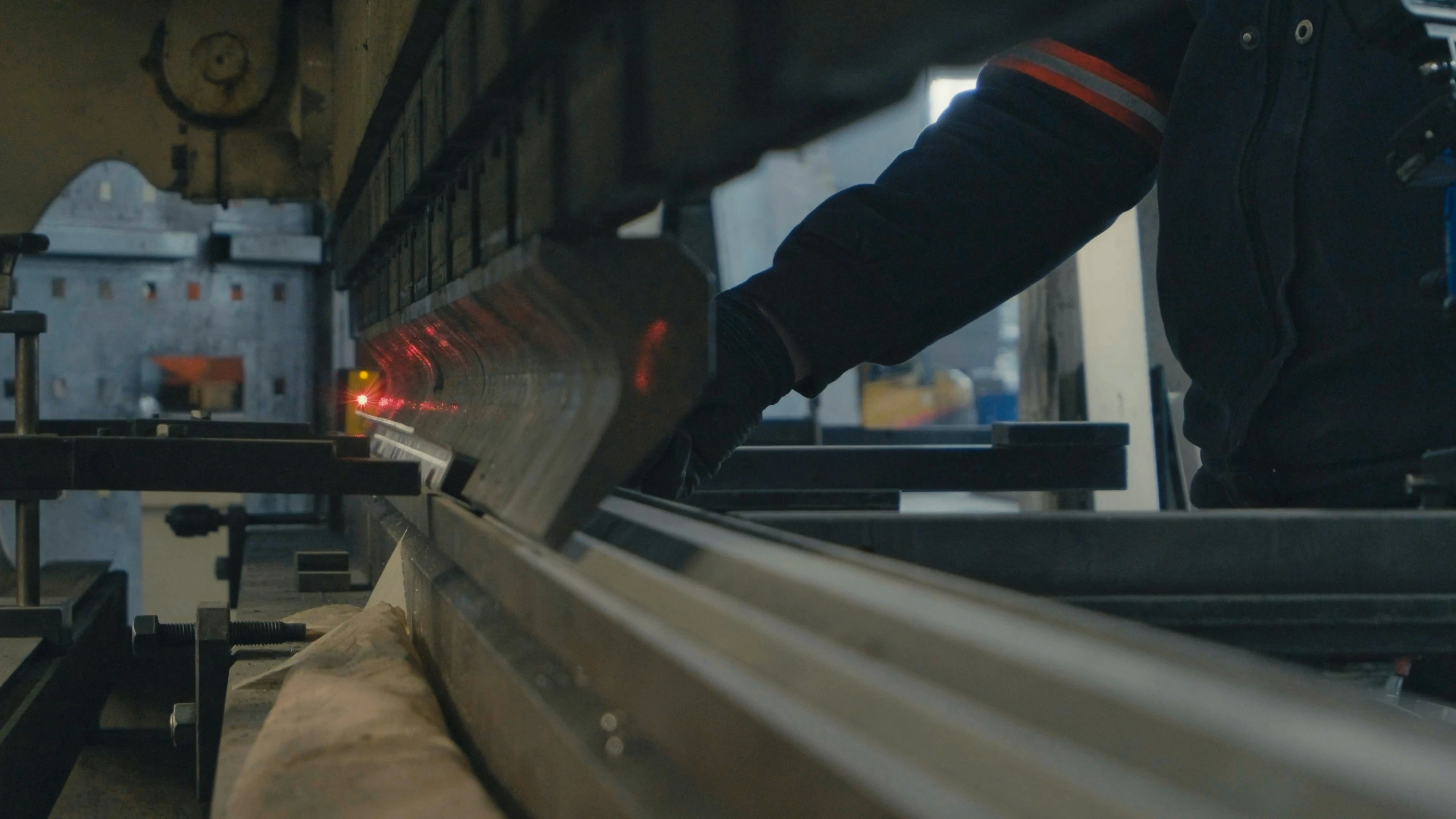 Gloved operator positioning a steel sheet in a press brake on a factory floor.