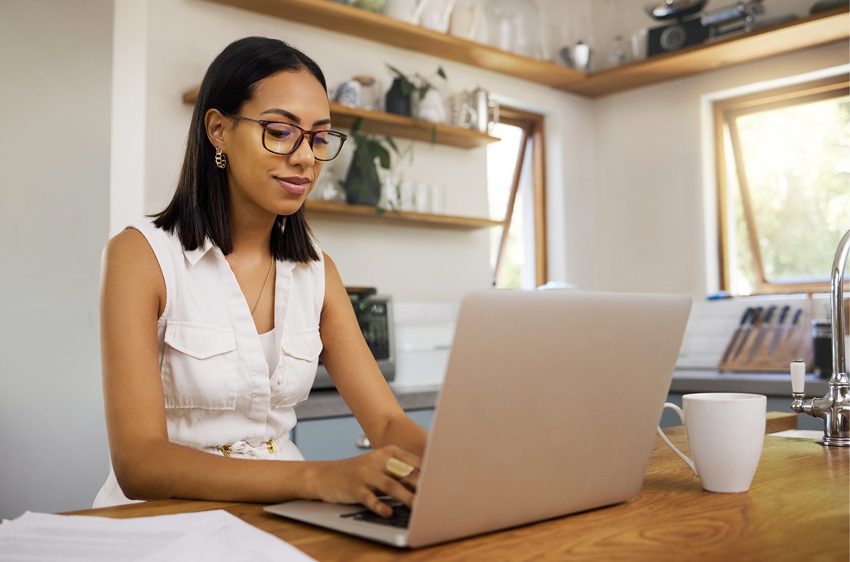 A talent recruiter with a soft smile working on her laptop in the office. The angle is on her face so we can't see what's is on the screen. She is wearing a blazer 