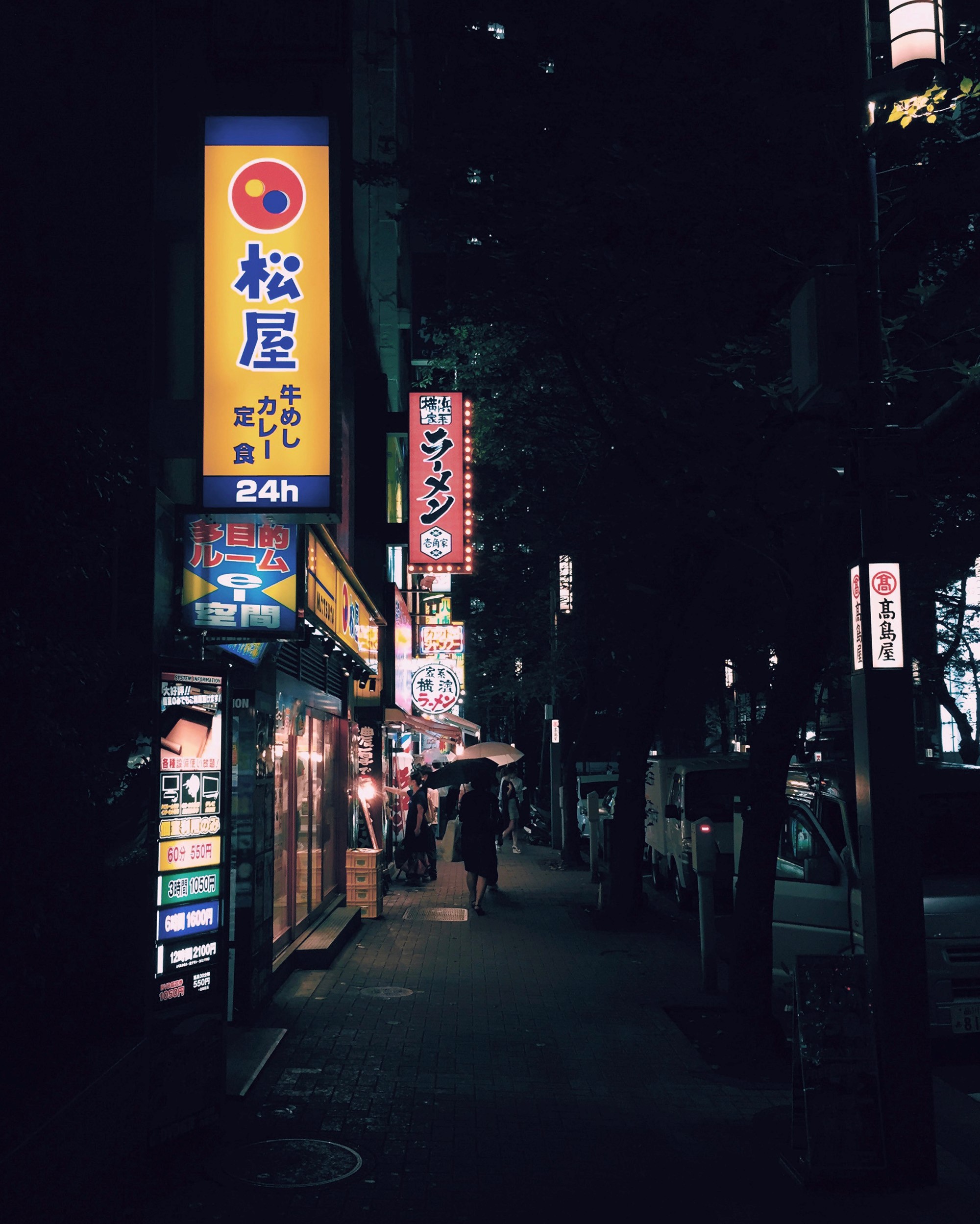 Narrow city street with glowing Japanese restaurant signs at night.