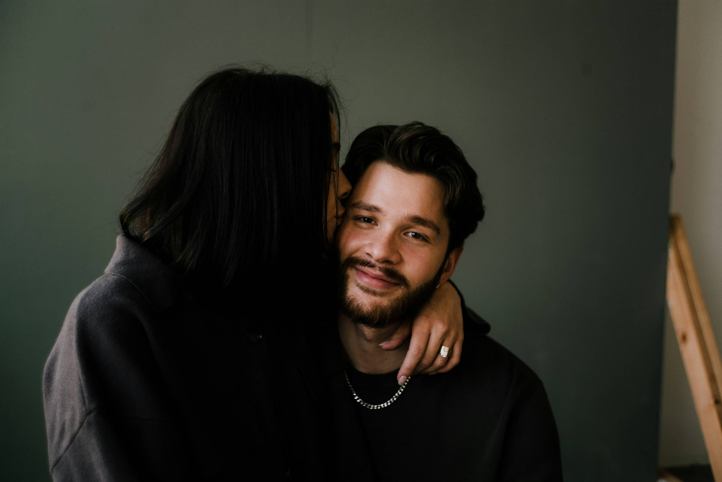 A woman kisses a man on the cheek in a studio setting
