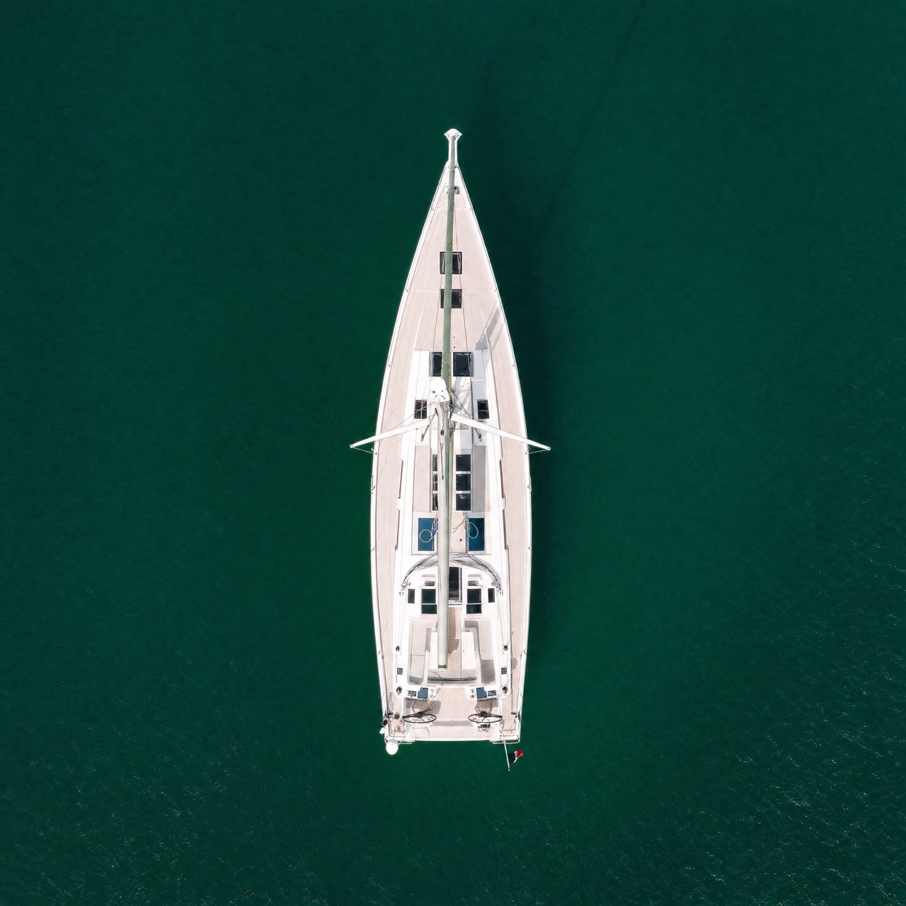 Overhead night aerial photograph of a Beneteau Clipper 361 sailing yacht with warm interior cabin lighting illuminating the teak deck, set against a dark black ocean background