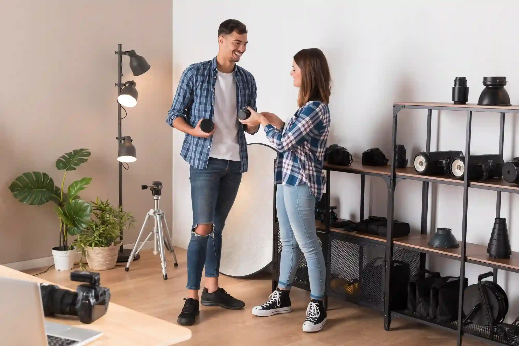 Two photographers in a professional studio discussing camera lenses while surrounded by photography lighting and equipment.