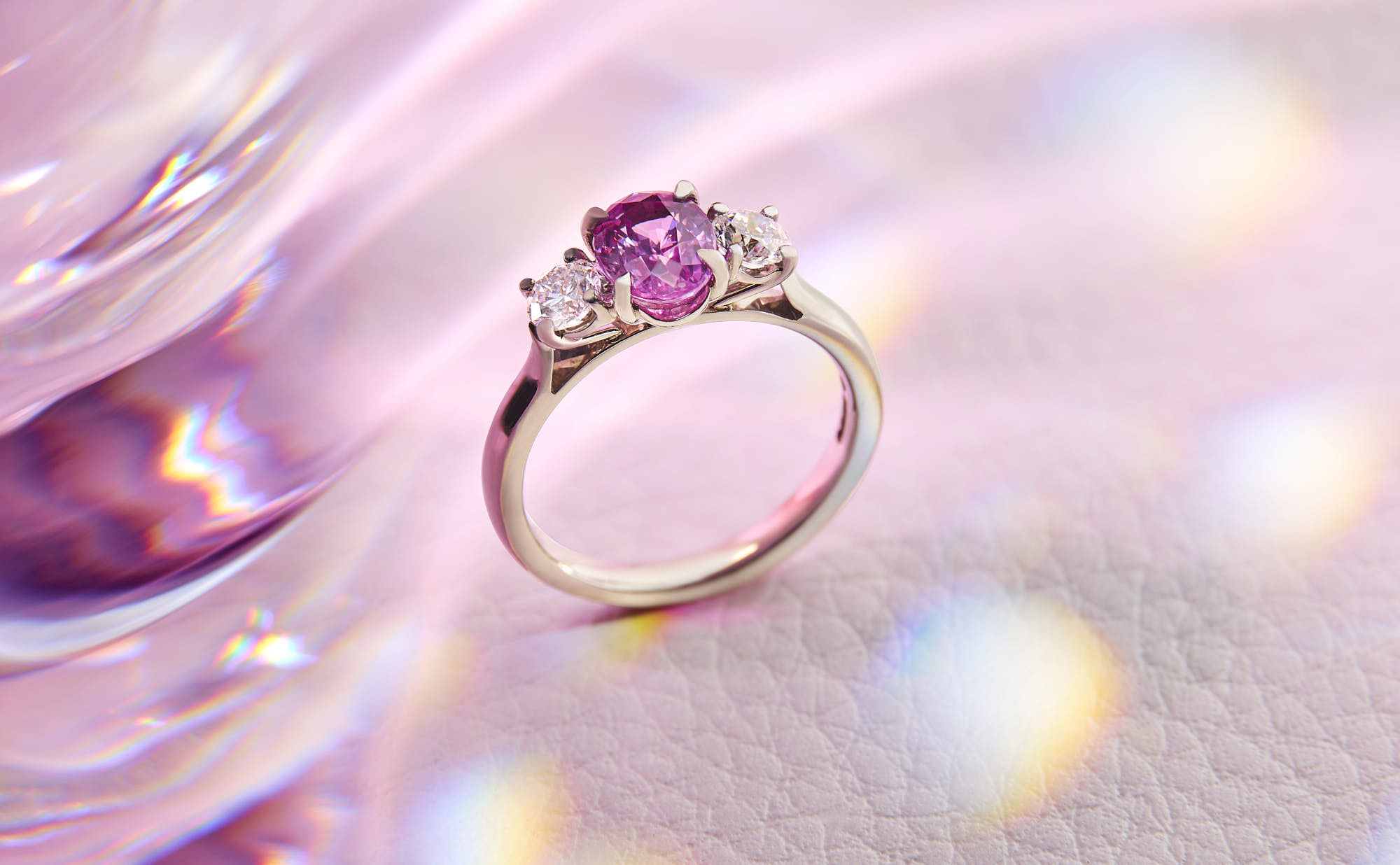 Elegant pink sapphire engagement ring with diamond accents on pink background.