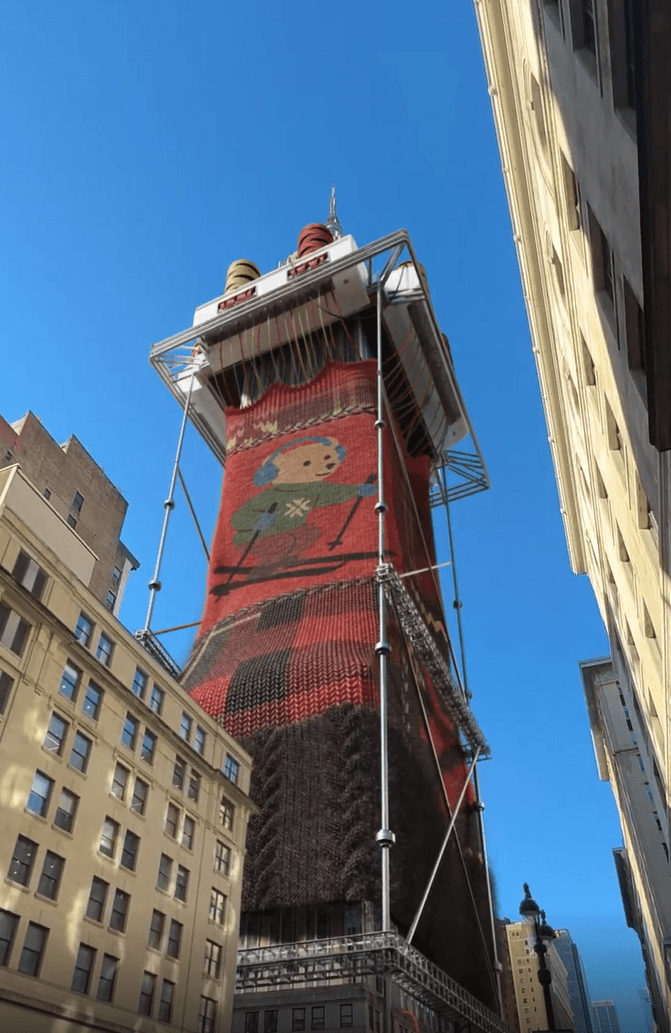 A tall building wrapped in a giant Ralph Lauren Polo Bear sweater in a city setting