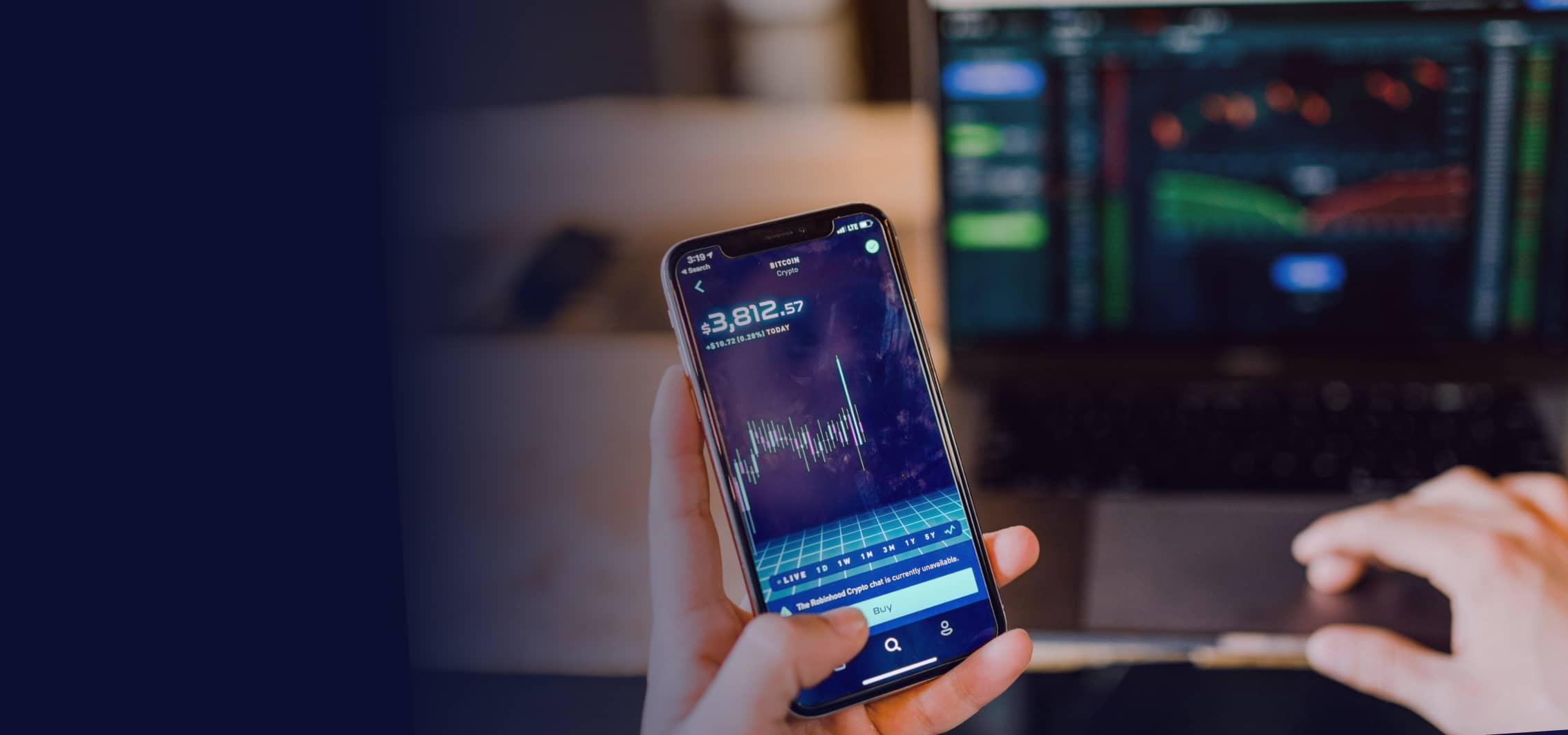 A person sitting in front of a laptop looking at stock charts and holding phone stocks.