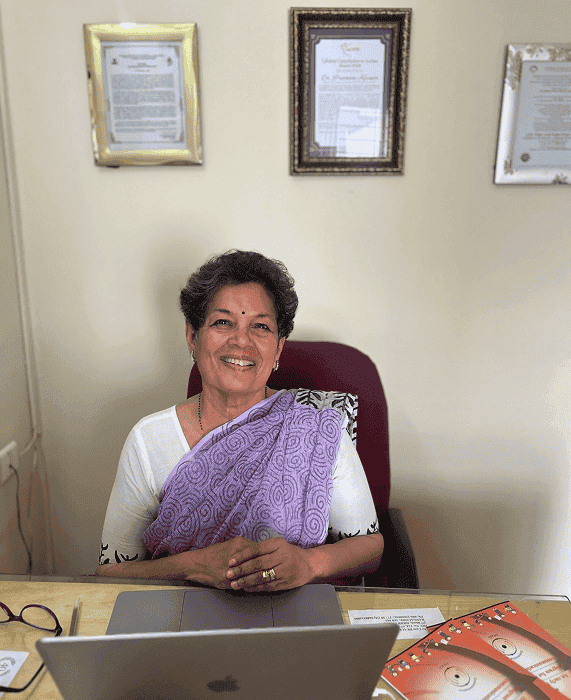 Smiling person with curly hair, wearing a black shirt, against a warm, dark background.