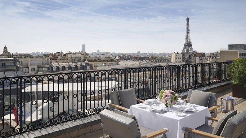 A rooftop dining setup overlooking the Paris skyline with a clear view of the Eiffel Tower, representing romance and refinement.  