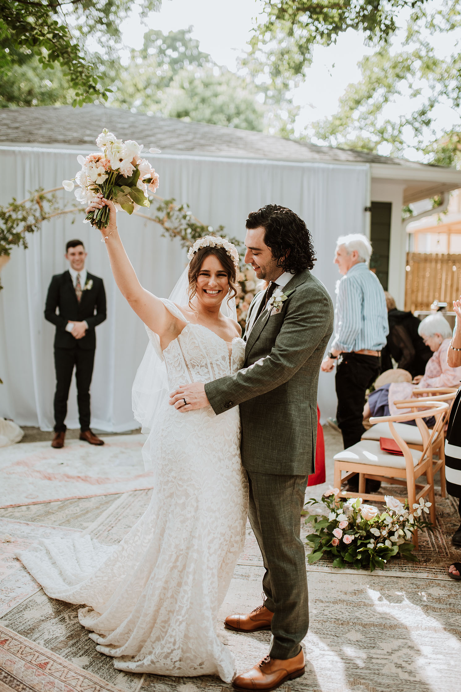 Bride and groom share a kiss beneath the ceremony arch surrounded by flowers.