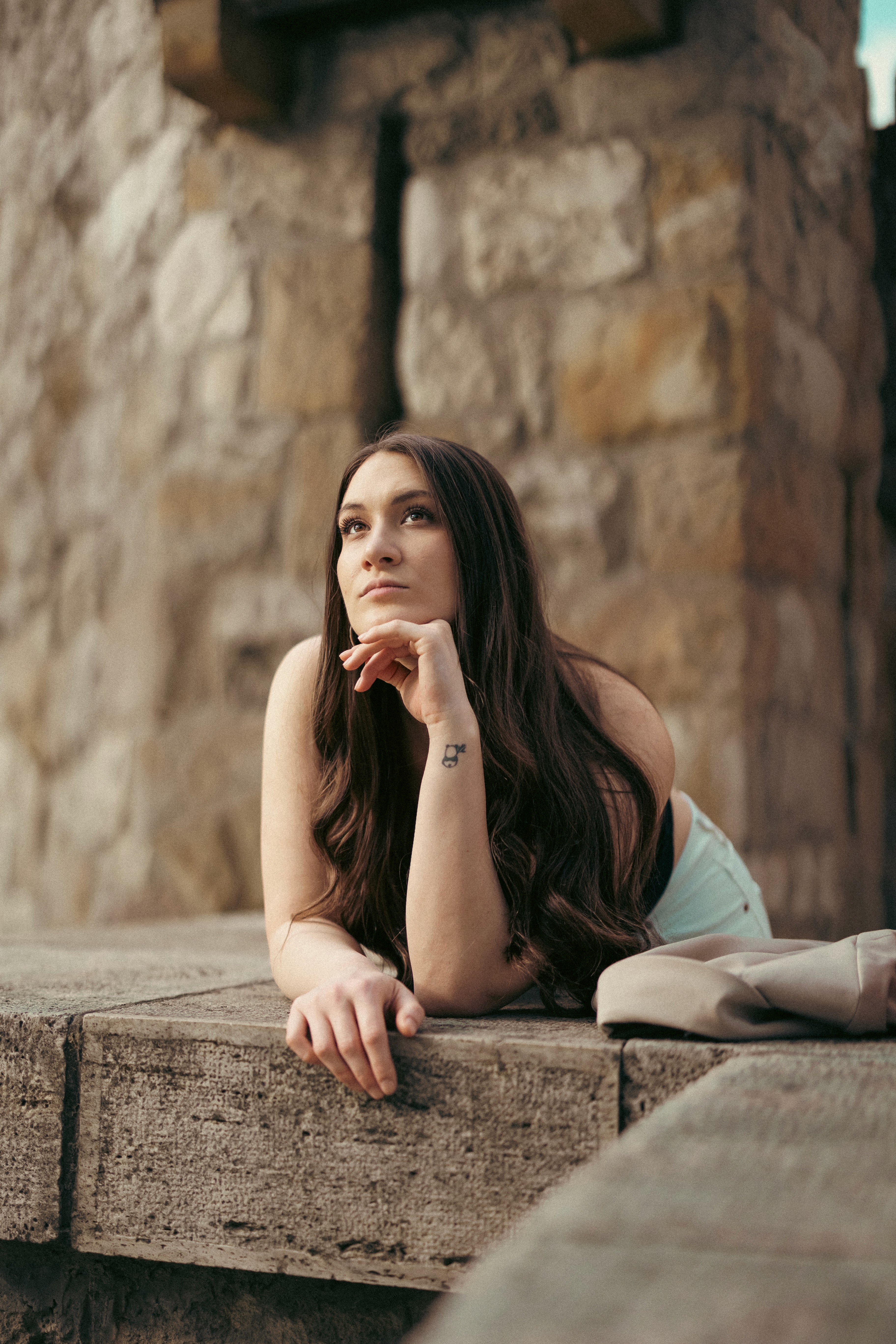 Elgondolkodó portré hosszú hajú nőről, aki kőlépcsőre támaszkodik a Vajdahunyad vára oszlopai között, Városliget Budapest