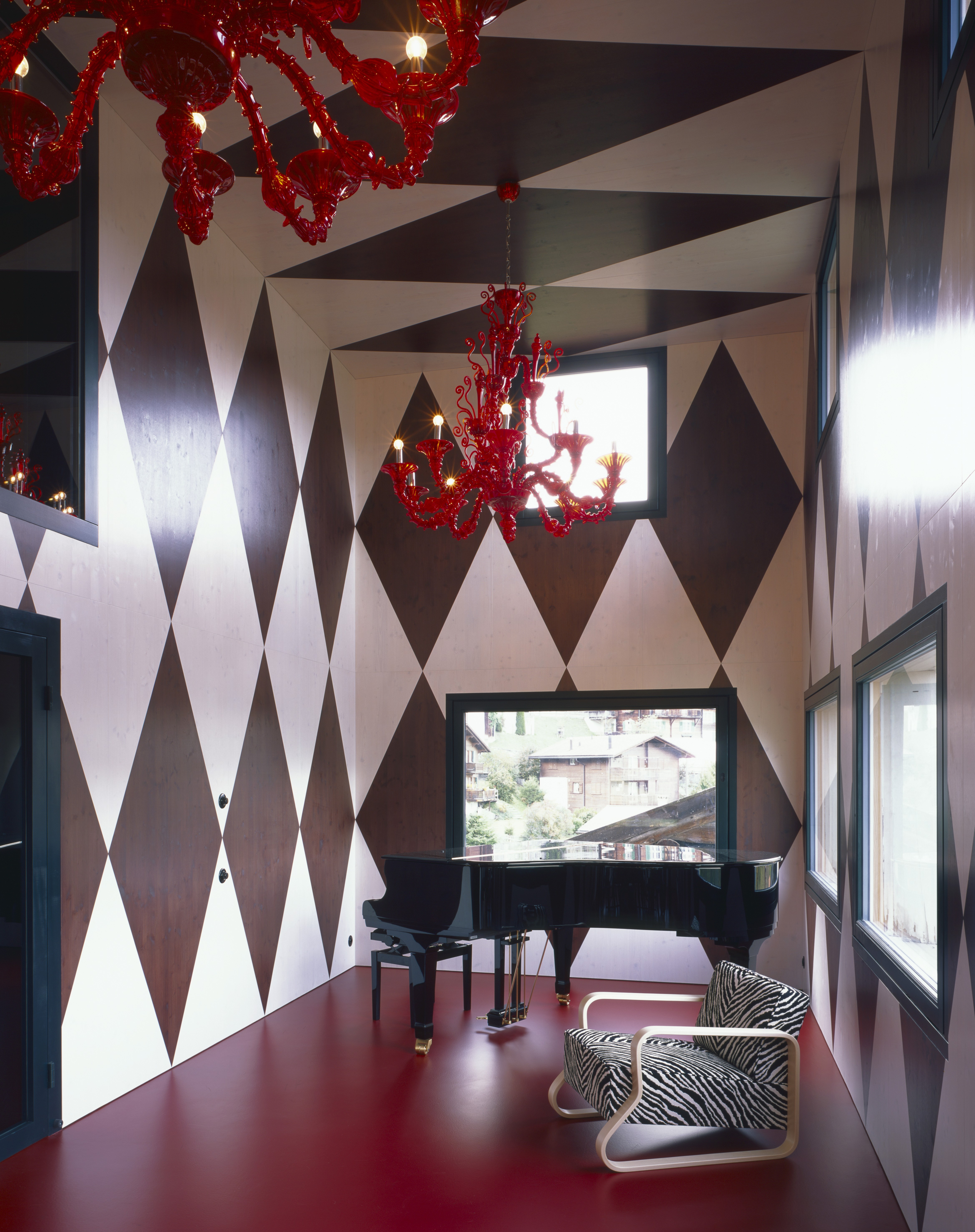 A piano in a room with tall ceilings and a red floor.