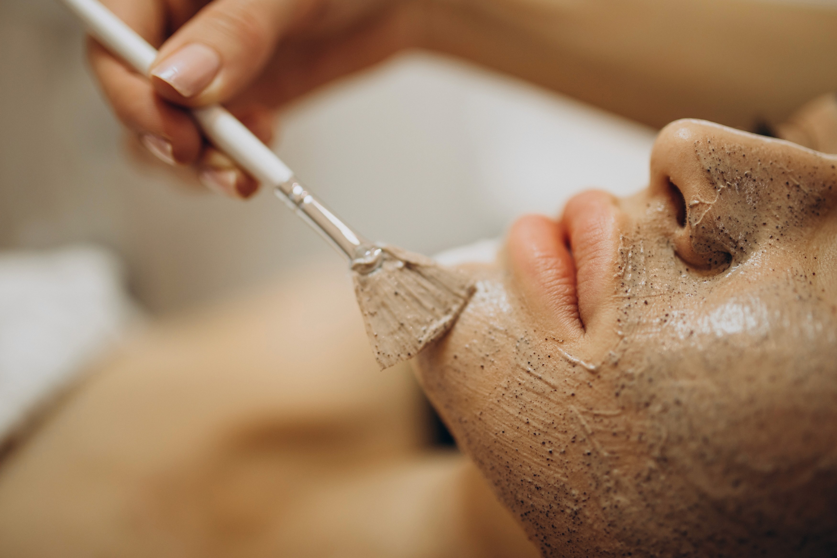 A woman lying down with a towel wrapped around her head, her face glowing with facial oil. She has a peaceful expression, enjoying a skincare treatment.