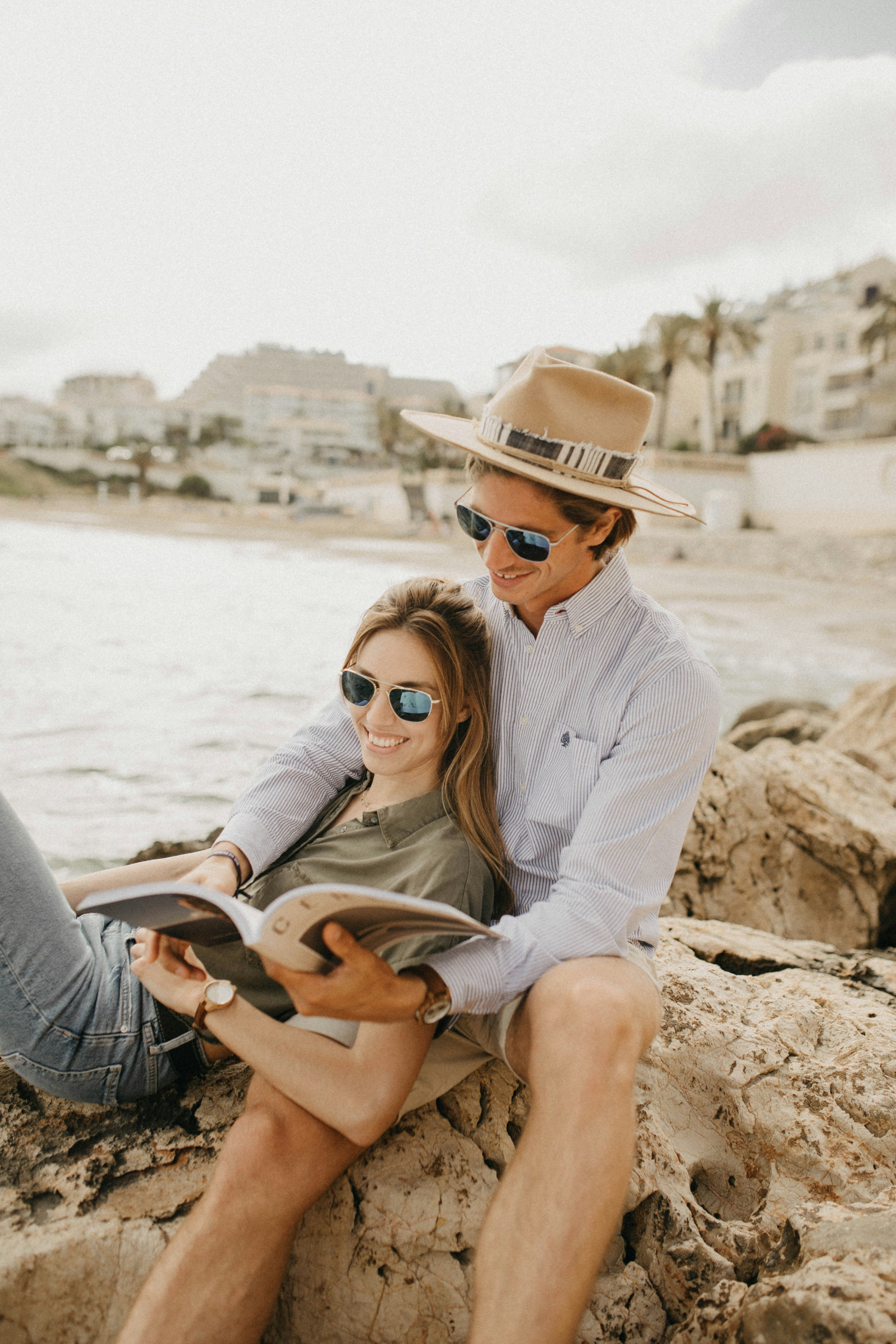 A man and a woman in aesthetic-toned clothing and aviator sunglasses are flipping through a magazine.