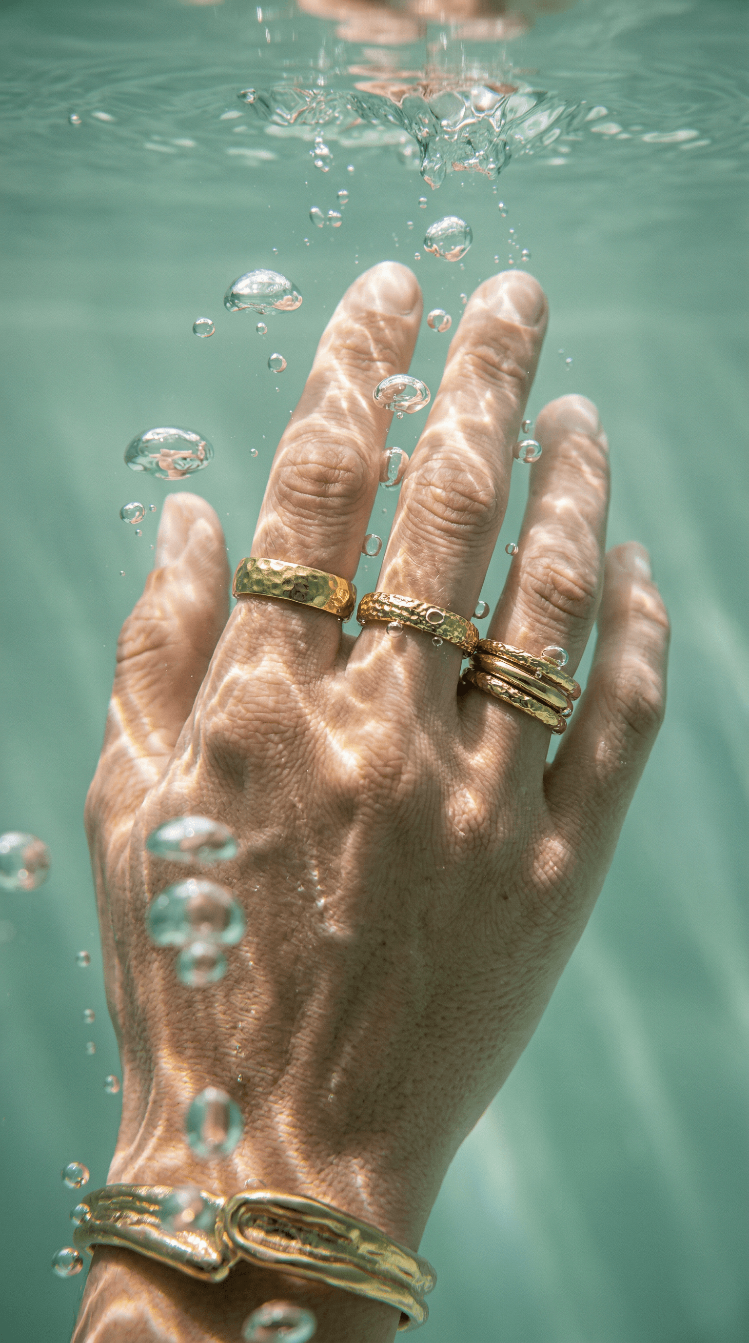 Underwater close-up of hand wearing hammered gold rings with bubbles and caustic light