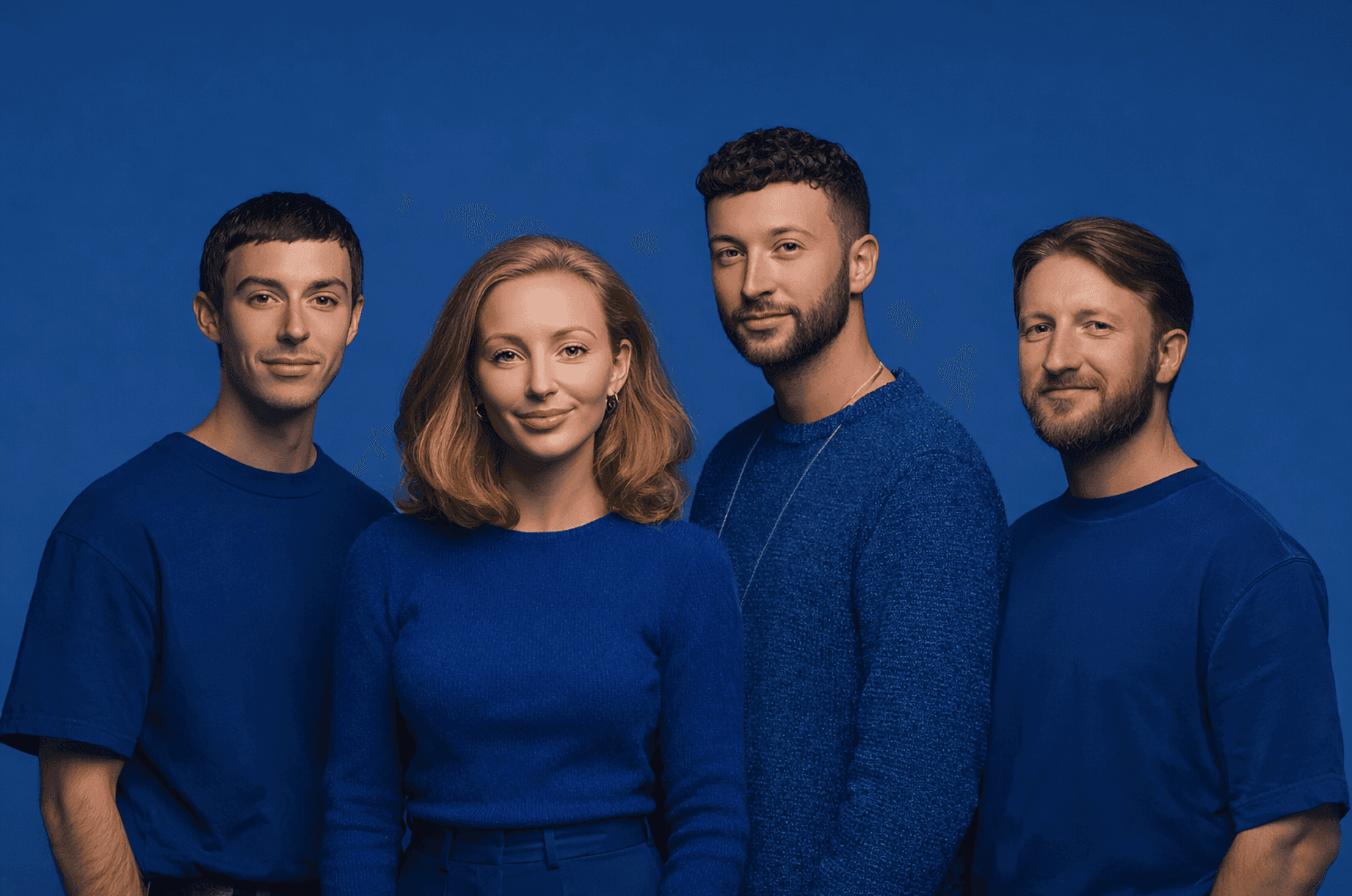 A group of four people wearing blue shirts, standing together and smiling for a photograph.