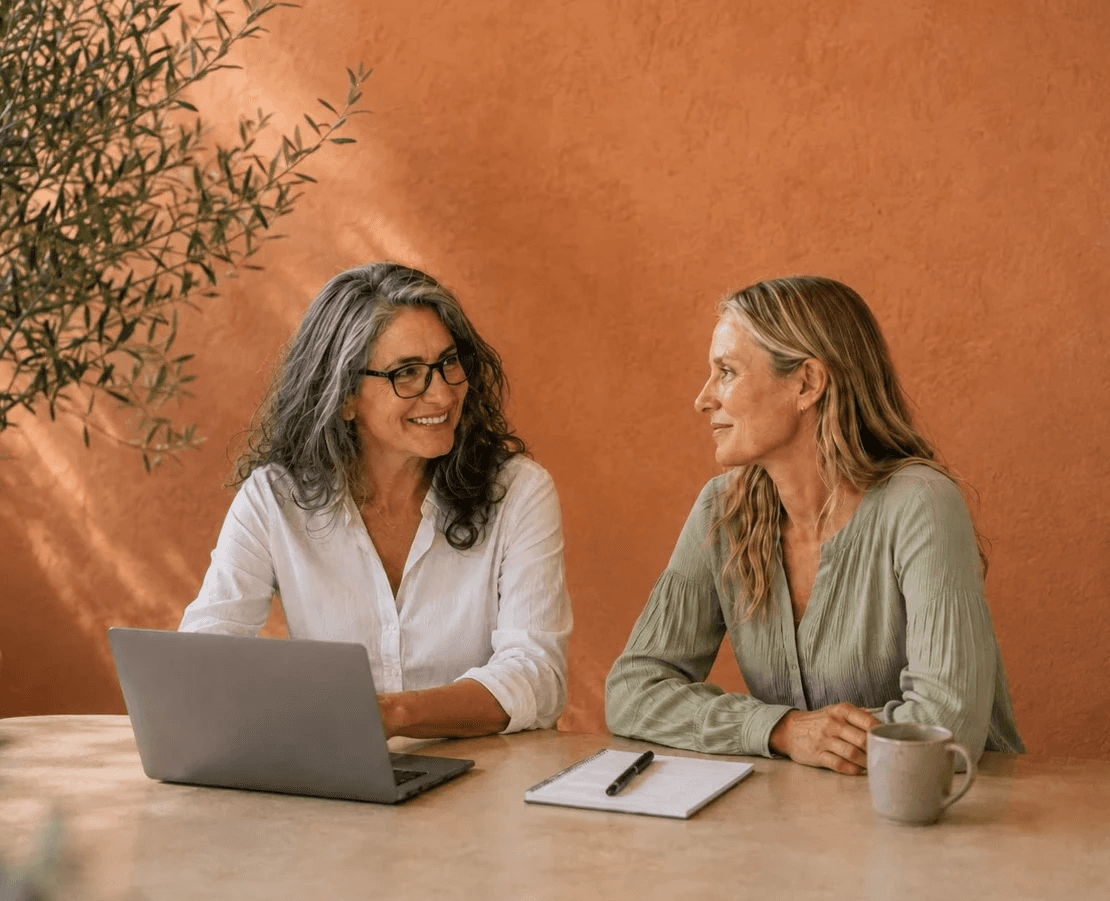 Two women in thier mid 40s, sitting in a sunny corporate setting, smiling and speaking with trust