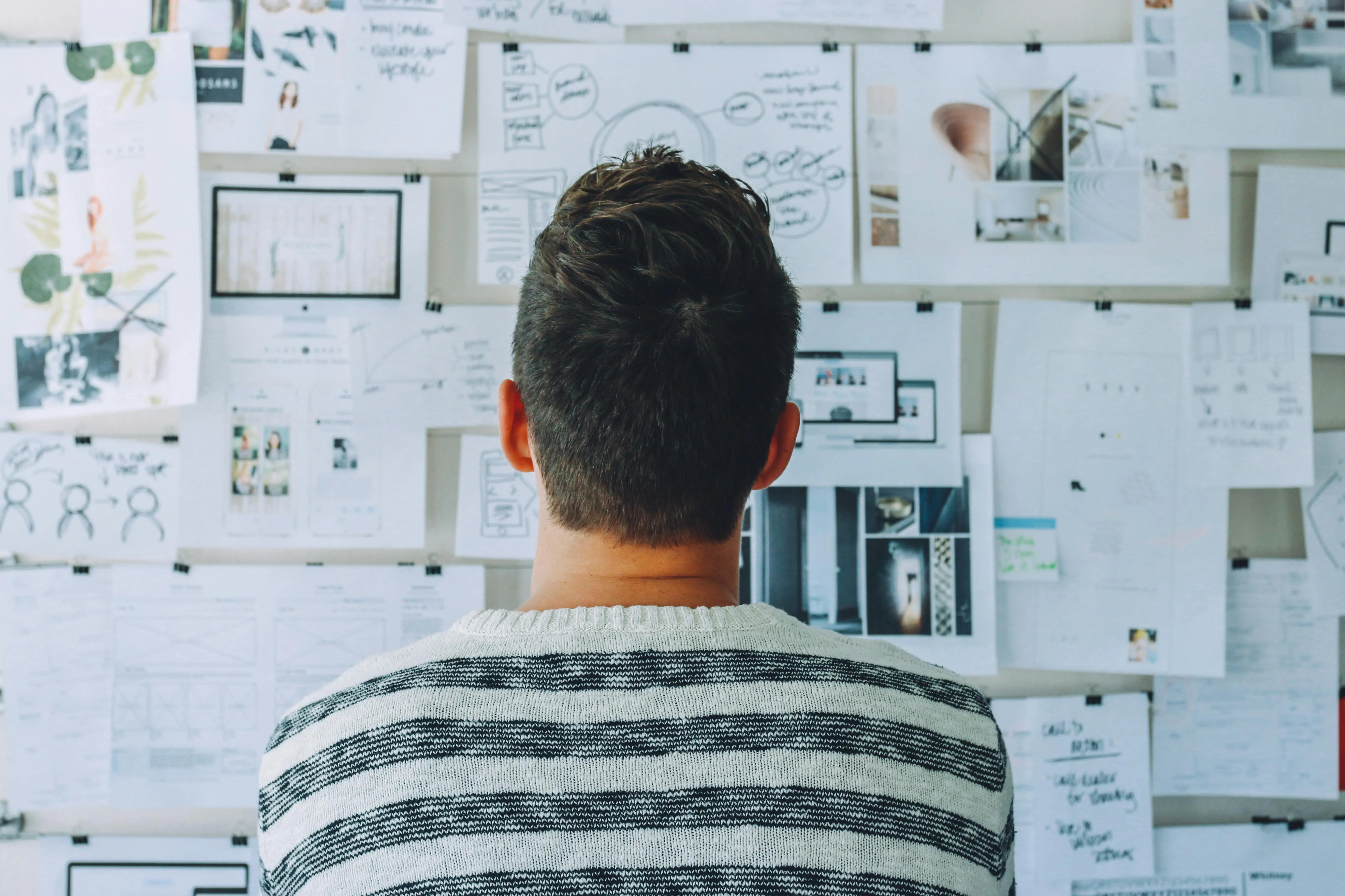 Person standing in front of a wall covered with papers, notes, and diagrams, planning and organizing ideas for a personal knowledge management system.