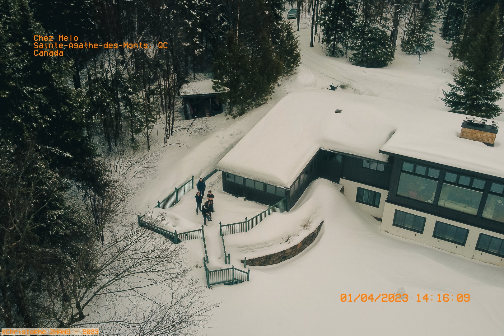 Vue aérienne d'une maison enneigée avec des personnes sortant dans la cour à Sainte-Agathe-des-Monts.