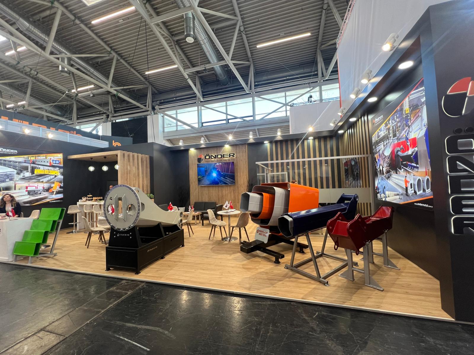 Önder Metal exhibition stand at Bauma 2025 Munich, featuring warm wooden finishes, black and grey brand surfaces, and illuminated Önder Metal branding.