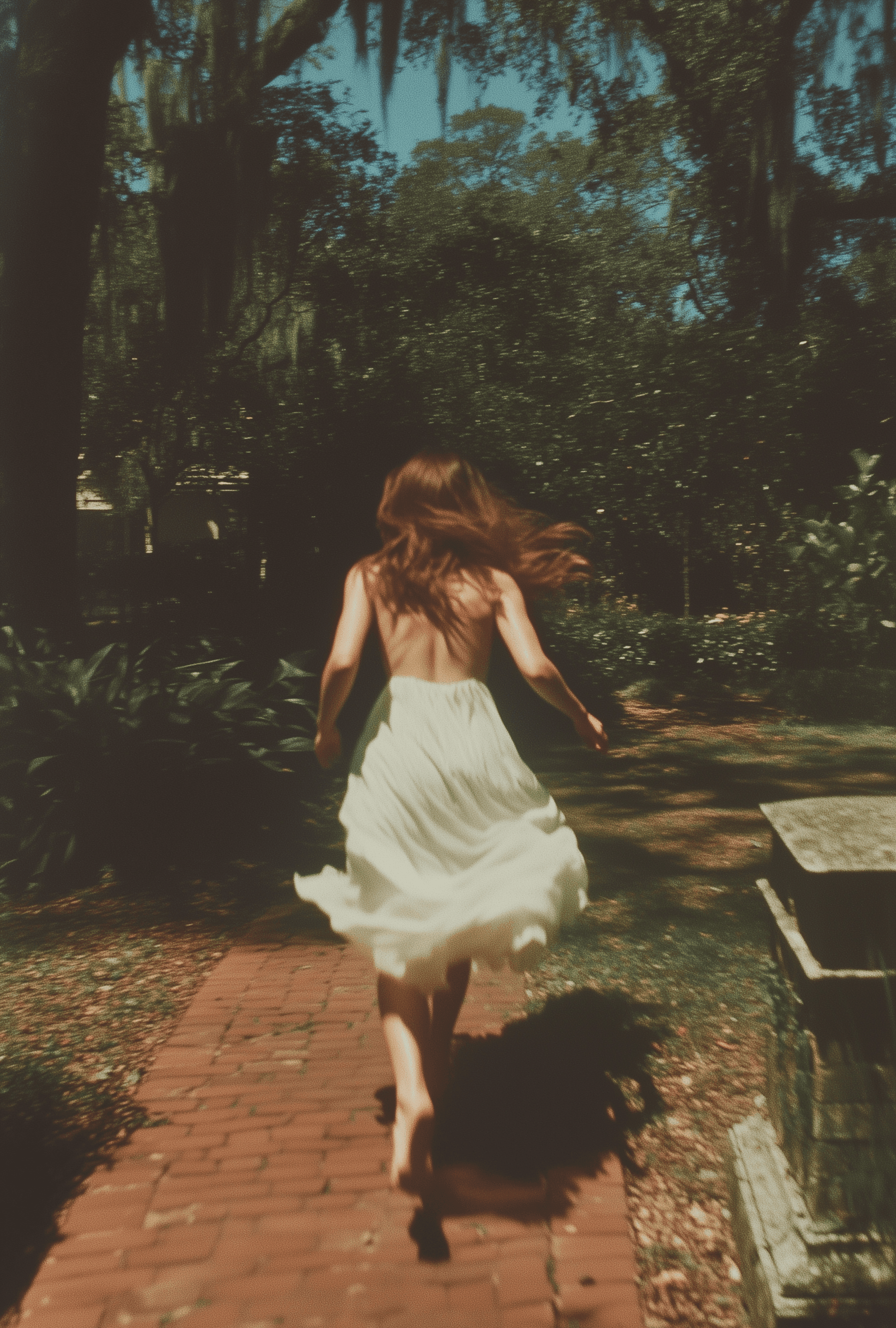 A photograph of an attractive woman running through the garden at Spanish Moss Manor, wearing a white dress and barefoot, with a blurry motion effect. Shot on Fujifilm Pro400H film stock with a flash.