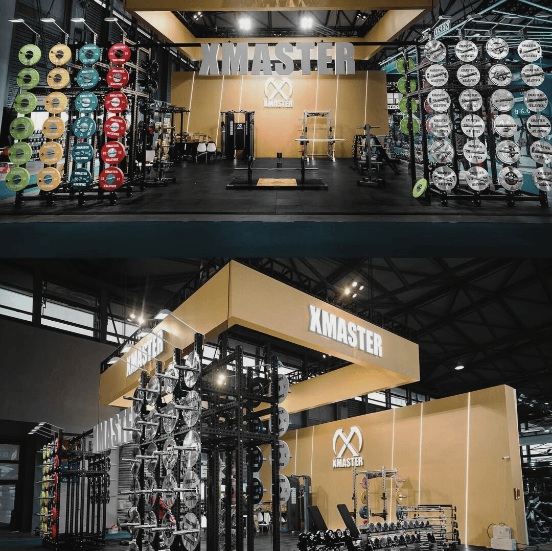 A muscular man smiling while performing a hanging leg raise on gymnastic rings in a bright fitness studio.