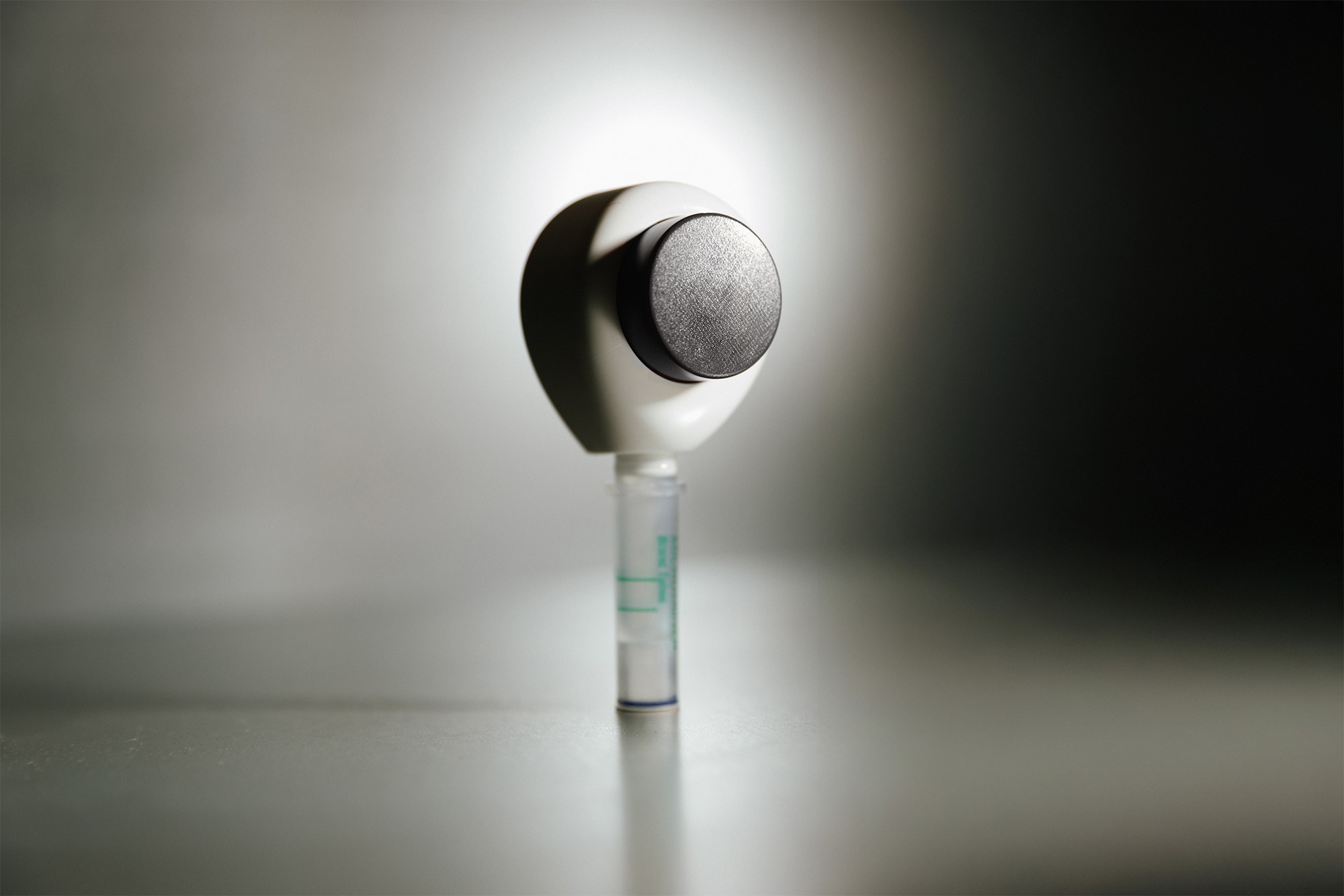 Rythm Health at-home testing device with a sample tube attached, shown against a clean, minimal background.