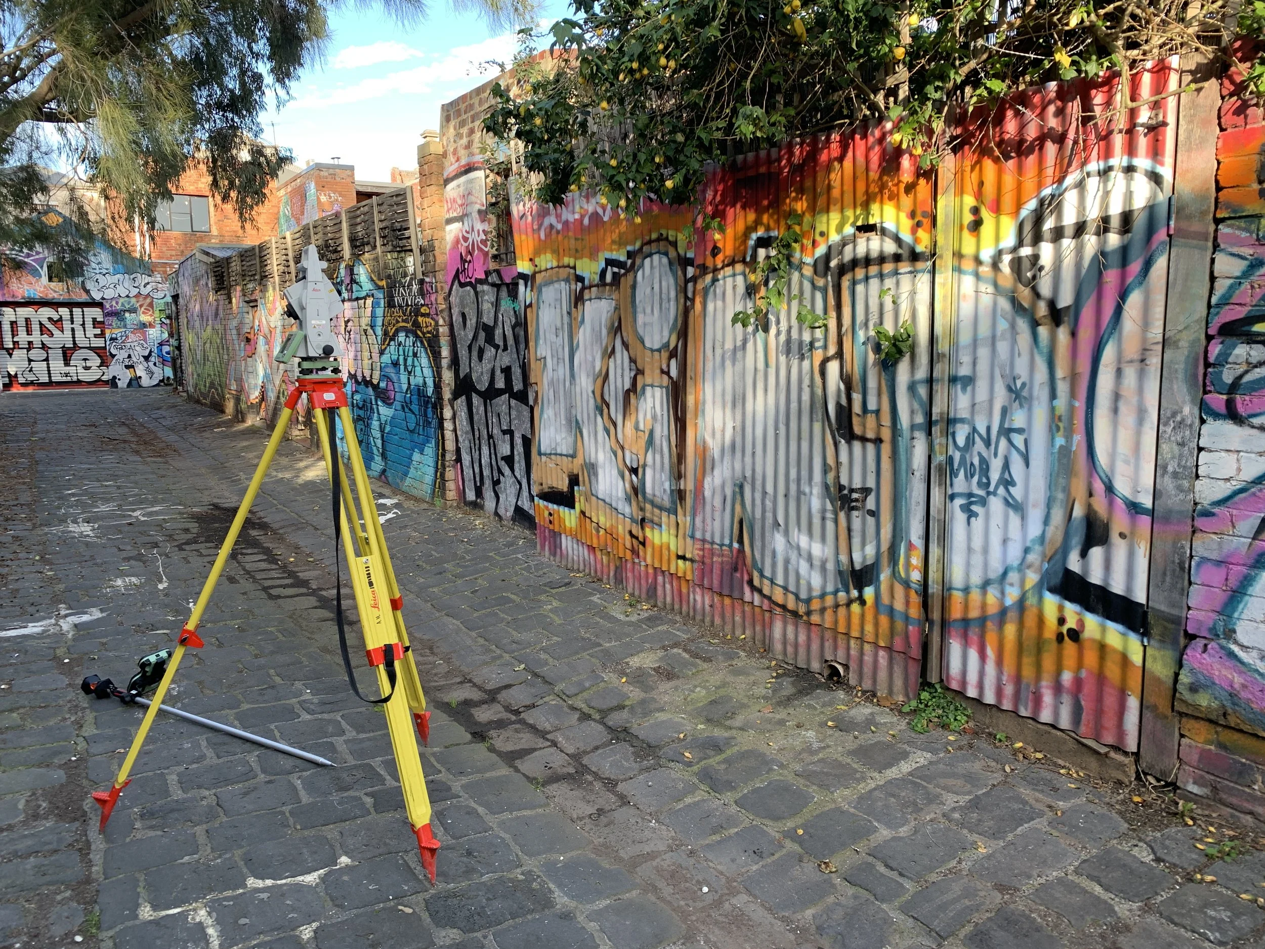 Professional surveying equipment set up in a Melbourne laneway with bright street art