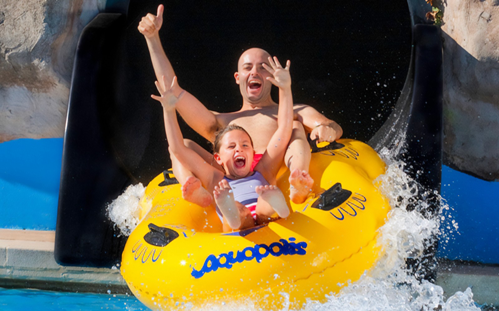 Father and child on a yellow raft sliding down a water slide at Aquopolis Cullera.