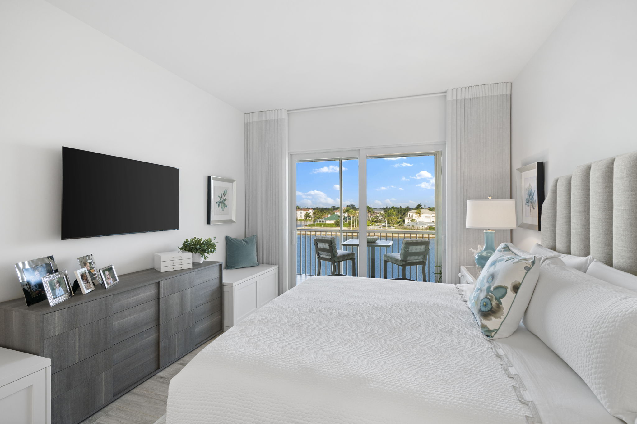 a medium sized white bedroom with windows looking out over the water