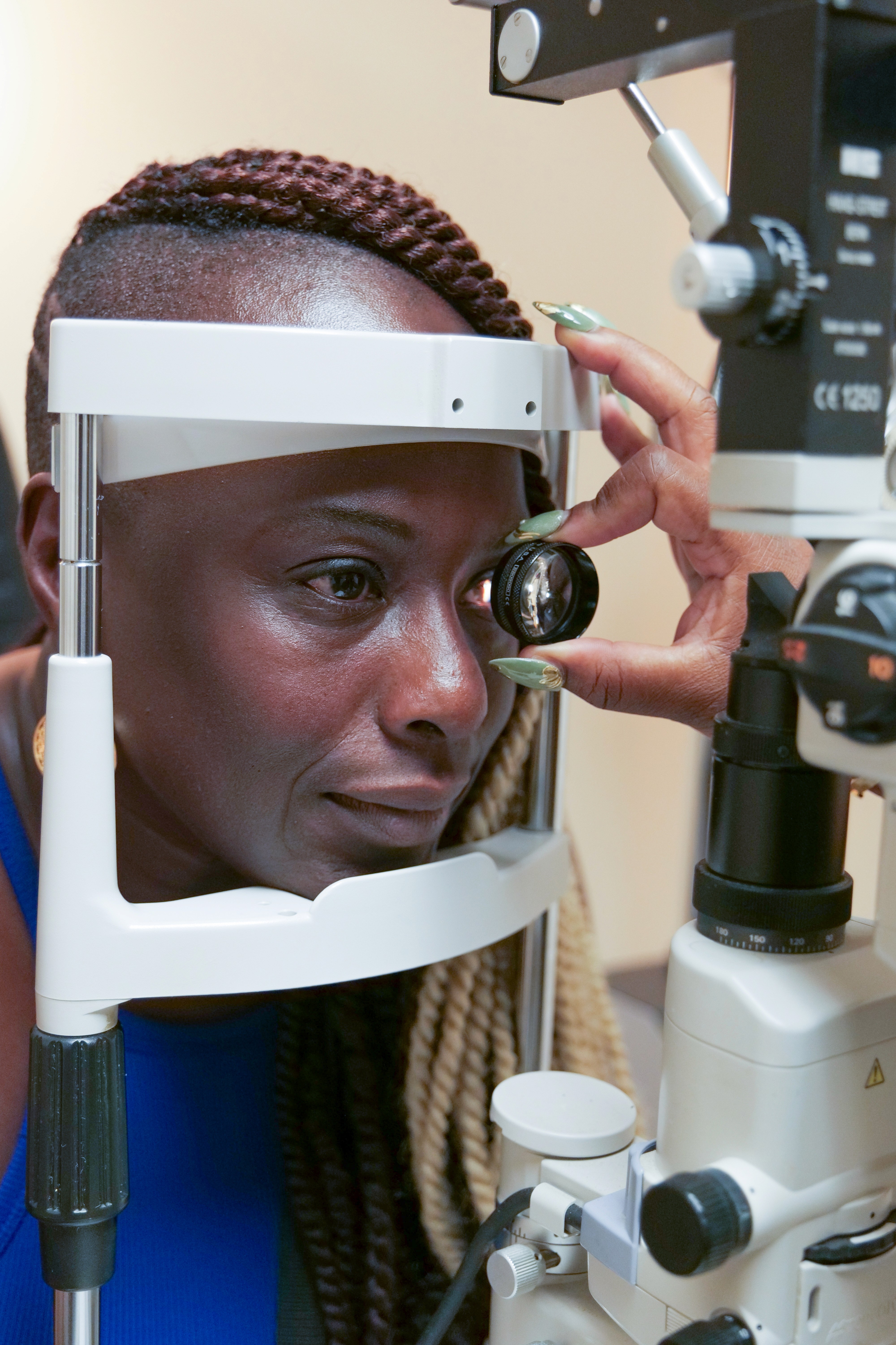 Patient undergoing eye examination with a slit lamp microscope as the optometrist inspects the eye using a handheld lens.