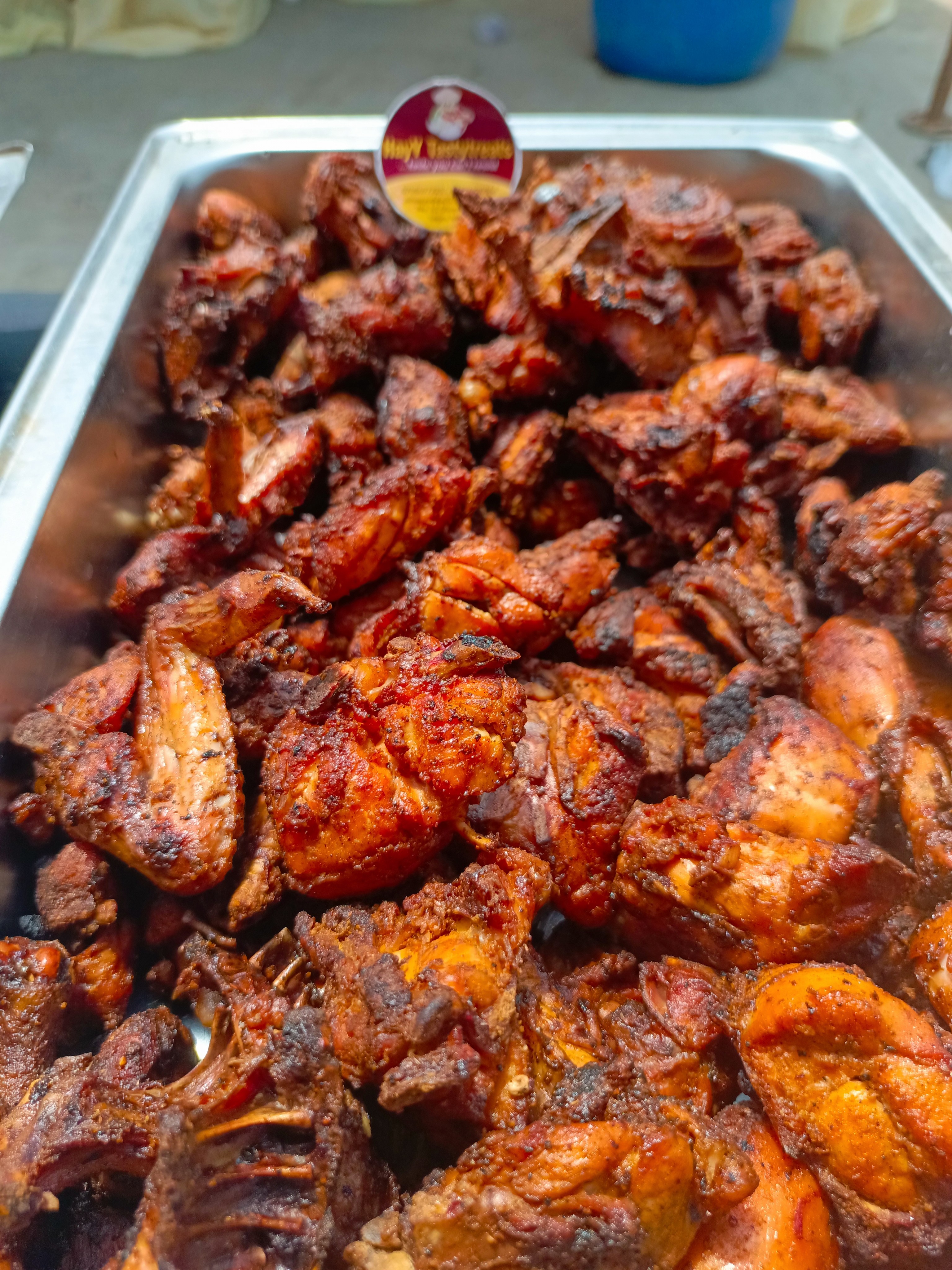 A large metal tray of roasted chicken pieces. The chicken is dark reddish-brown and appears seasoned.