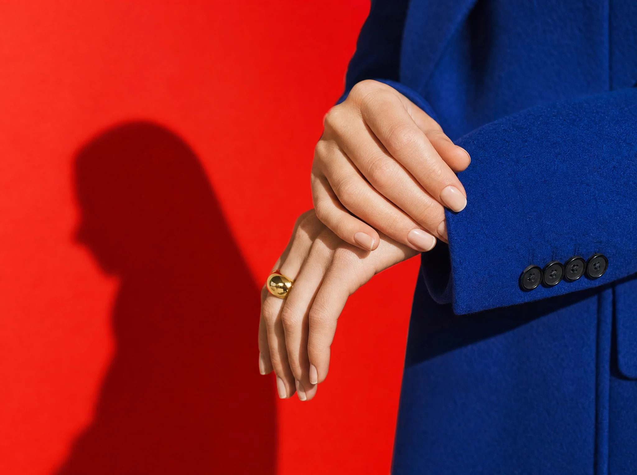 Hand with a gold ring resting on a cobalt sleeve against red, Maison Oro
