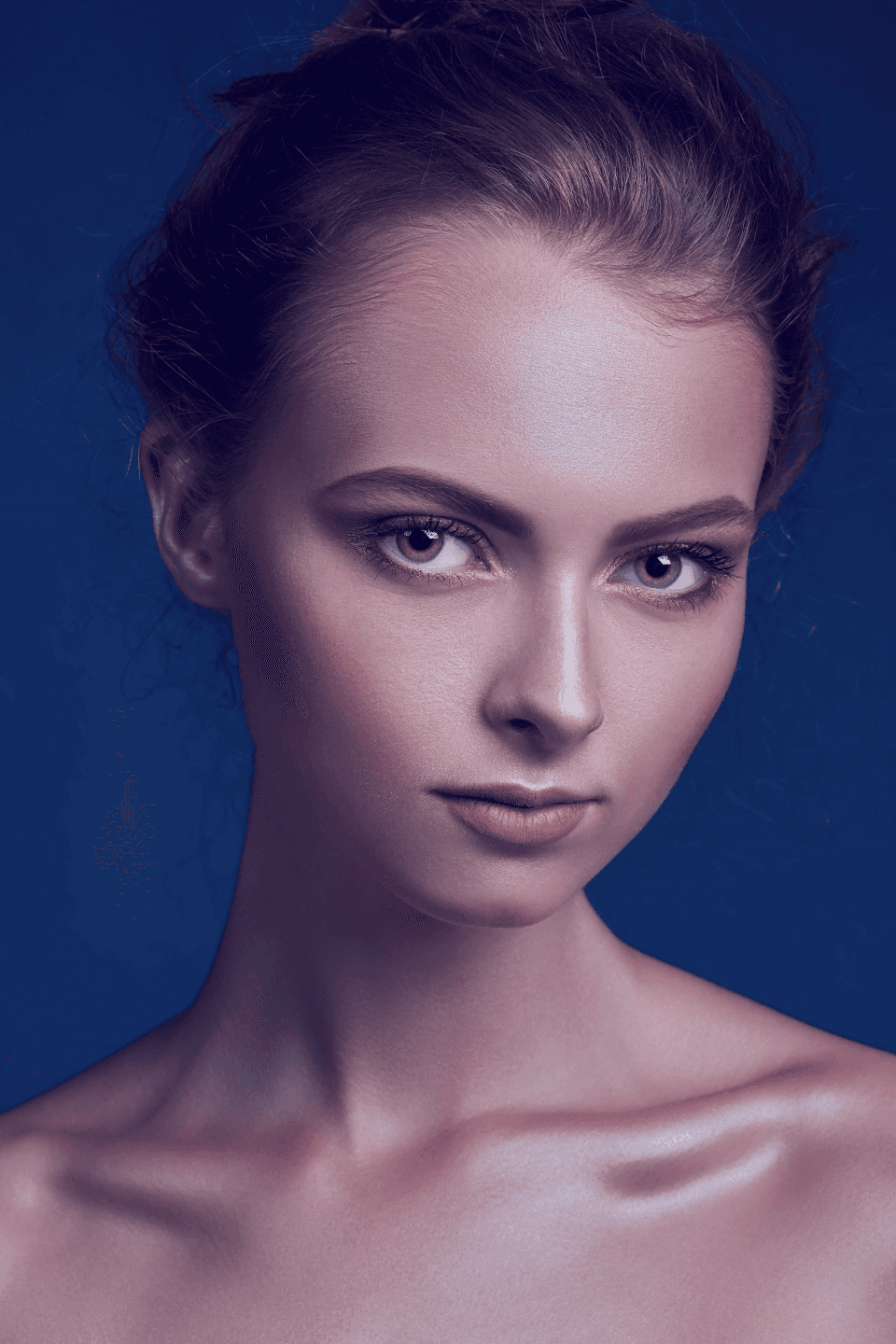 A portrait of a person with an updo hairstyle and natural makeup, set against a deep blue background. (Background Removed)