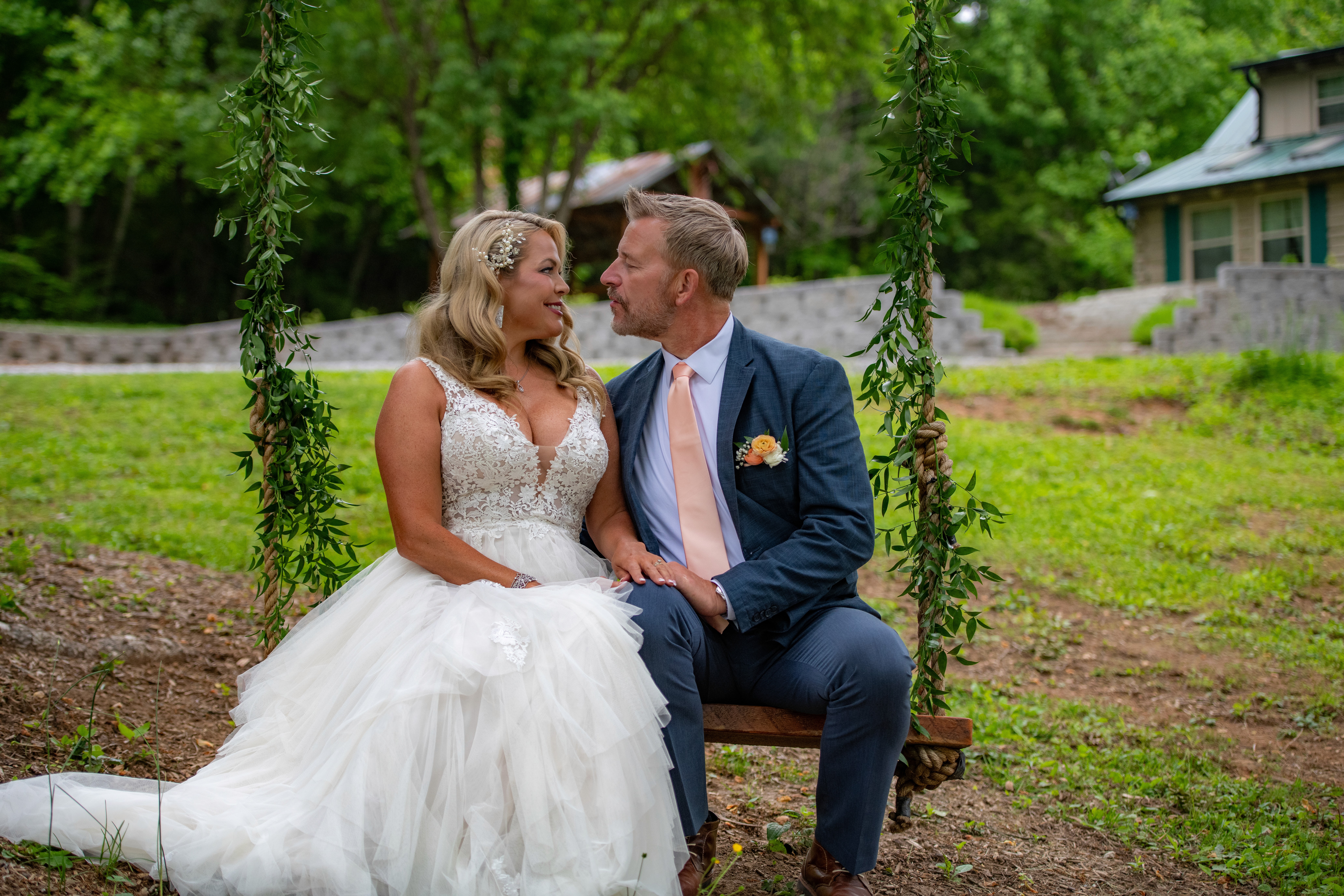 Newlyweds smile at each other while seated on a swing, the bride in a white gown and the groom in a suit.